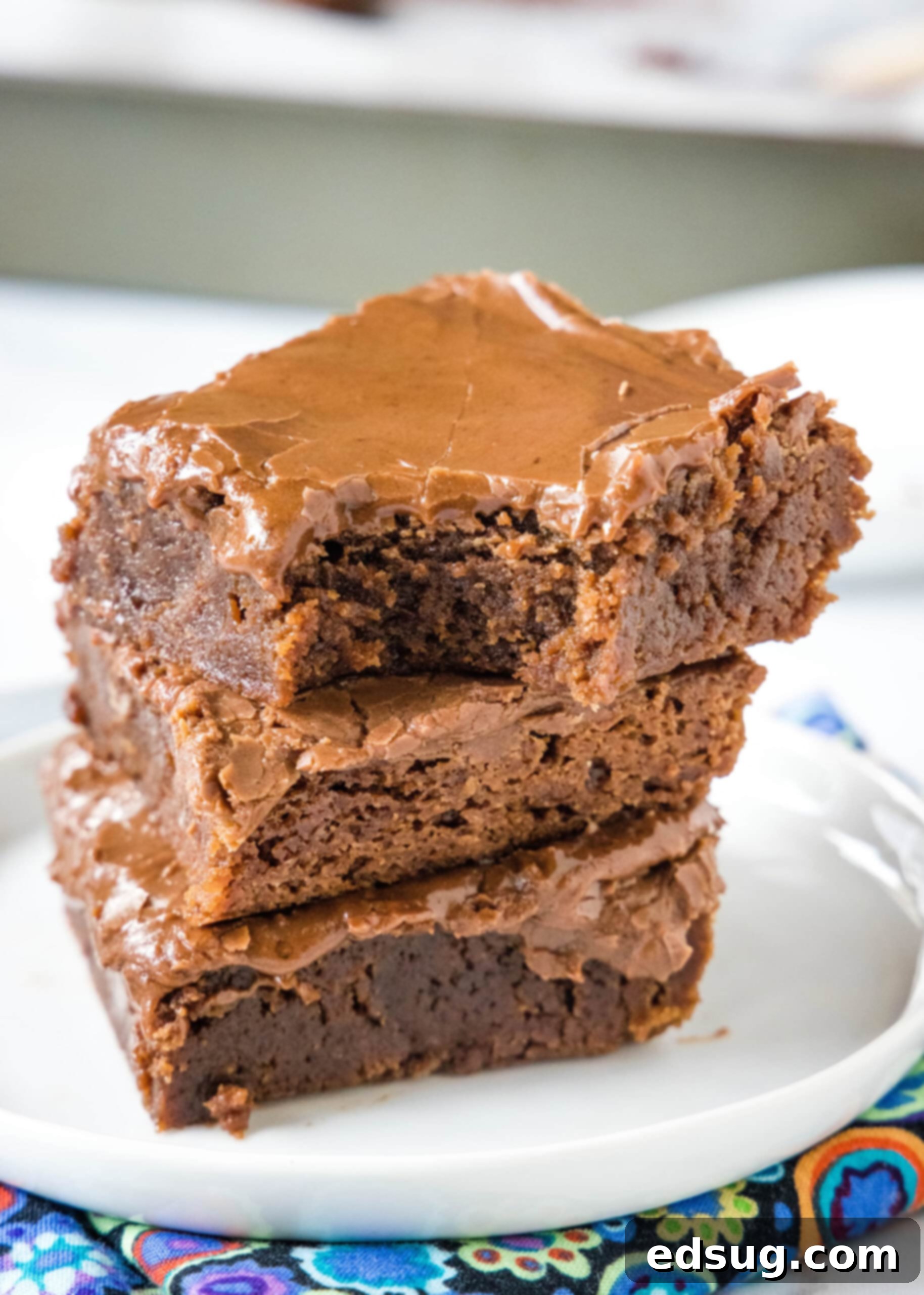 Lunch lady brownies are moist, fudgy brownies just like the ones served at school lunches! Every bite is filled with chocolate flavor. Three perfectly cut squares of lunch lady brownies stacked on a white plate, with a bite missing from the top brownie, revealing its fudgy texture.