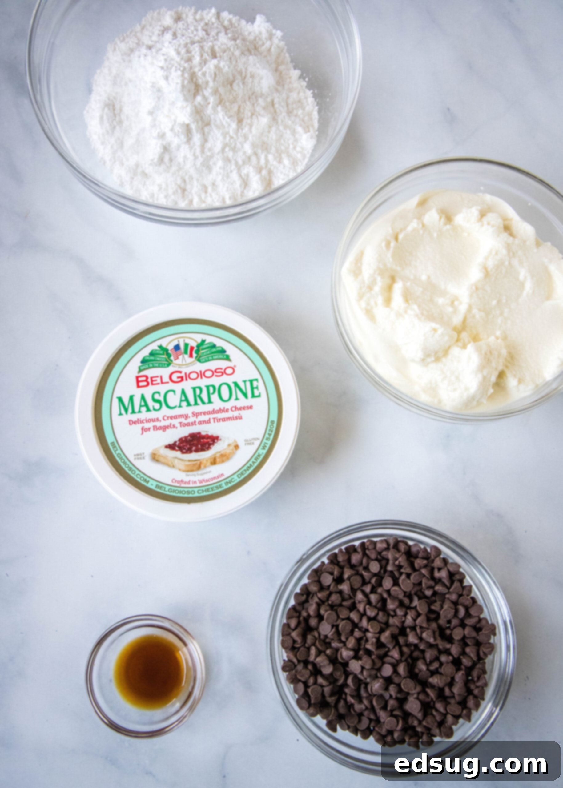 An overhead shot showcasing all the essential ingredients laid out for making delicious cannoli dip: ricotta cheese, mascarpone, powdered sugar, vanilla extract, and mini chocolate chips.