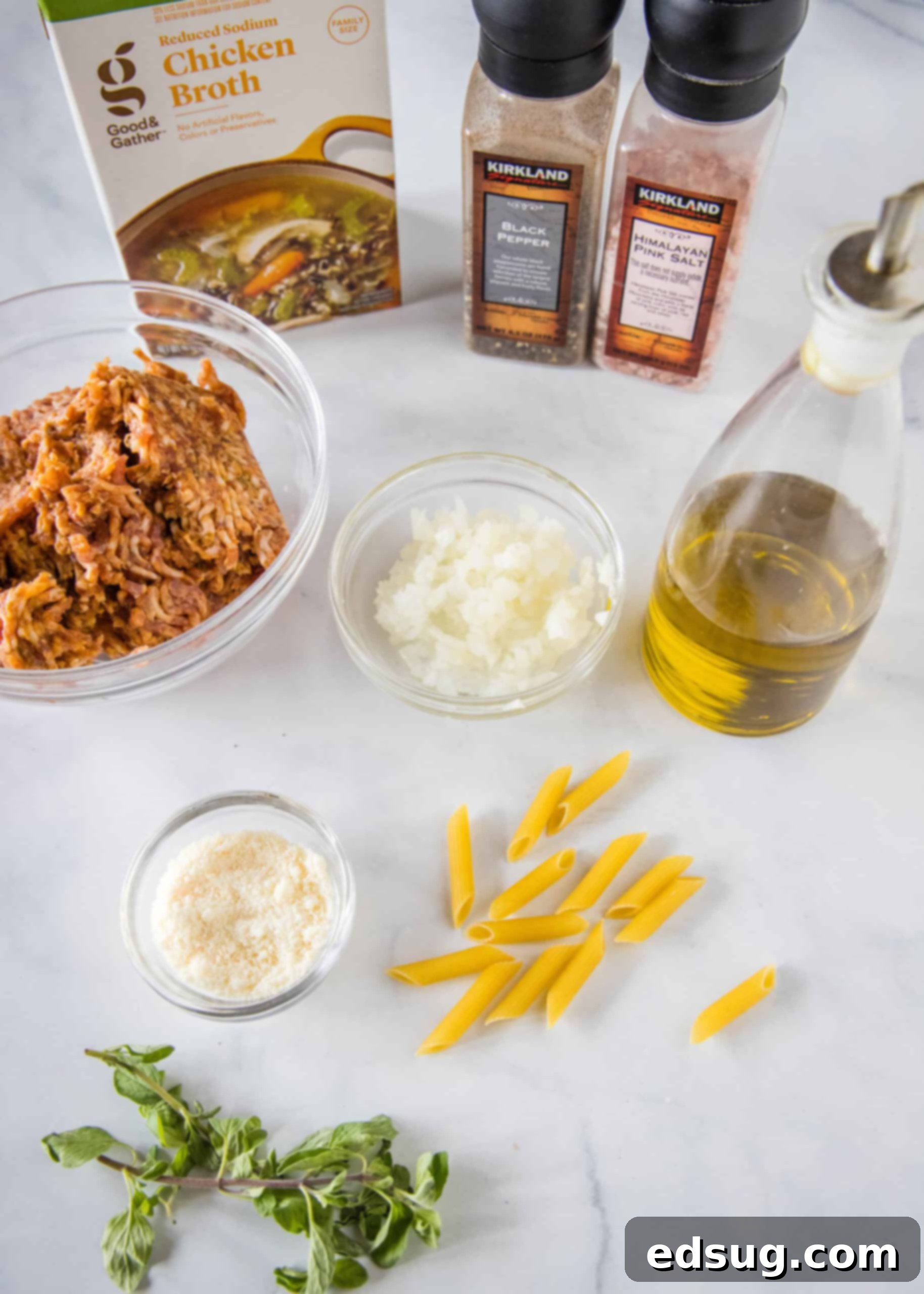Ingredients for homemade Pasta Risotto. A collection of fresh ingredients laid out, including penne pasta, Italian sausage, onion, broth, parmesan, and oregano, ready for making pasta risotto.