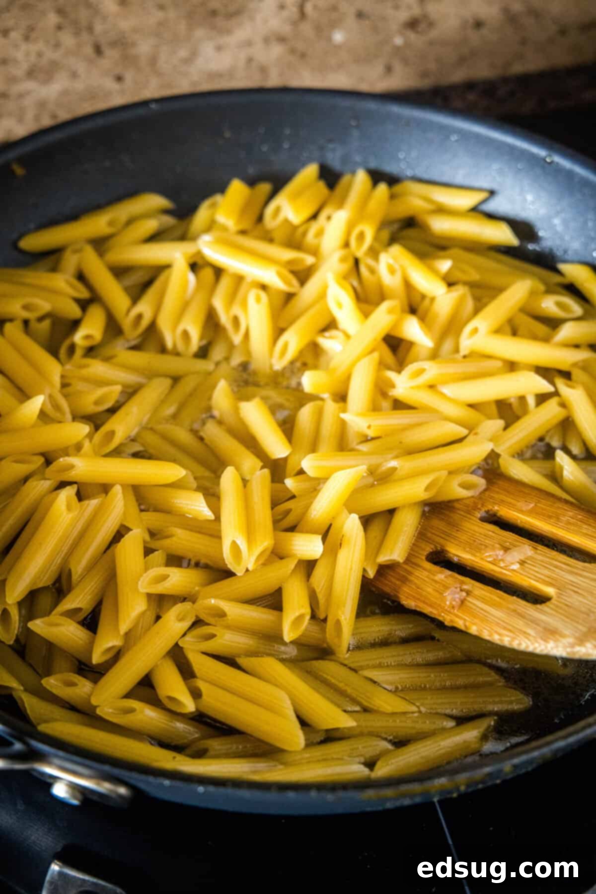 Penne pasta cooking risotto-style in broth. Penne pasta being gradually cooked in chicken broth in a skillet, absorbing the liquid to create a creamy sauce.