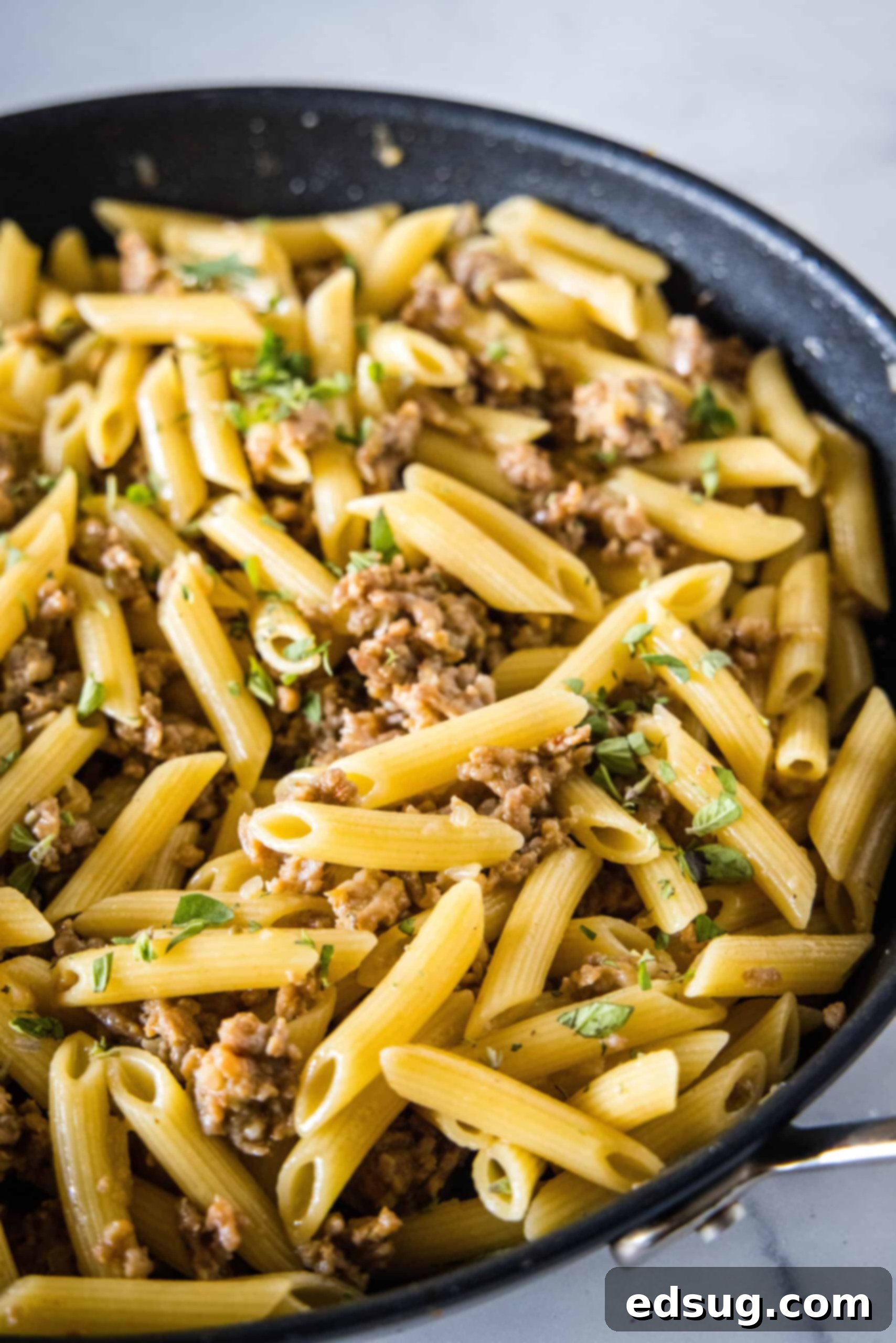 Creamy Pasta Risotto in a skillet. A close-up view of creamy pasta risotto in a cast iron skillet, showcasing its rich texture, penne pasta, and crumbled Italian sausage.