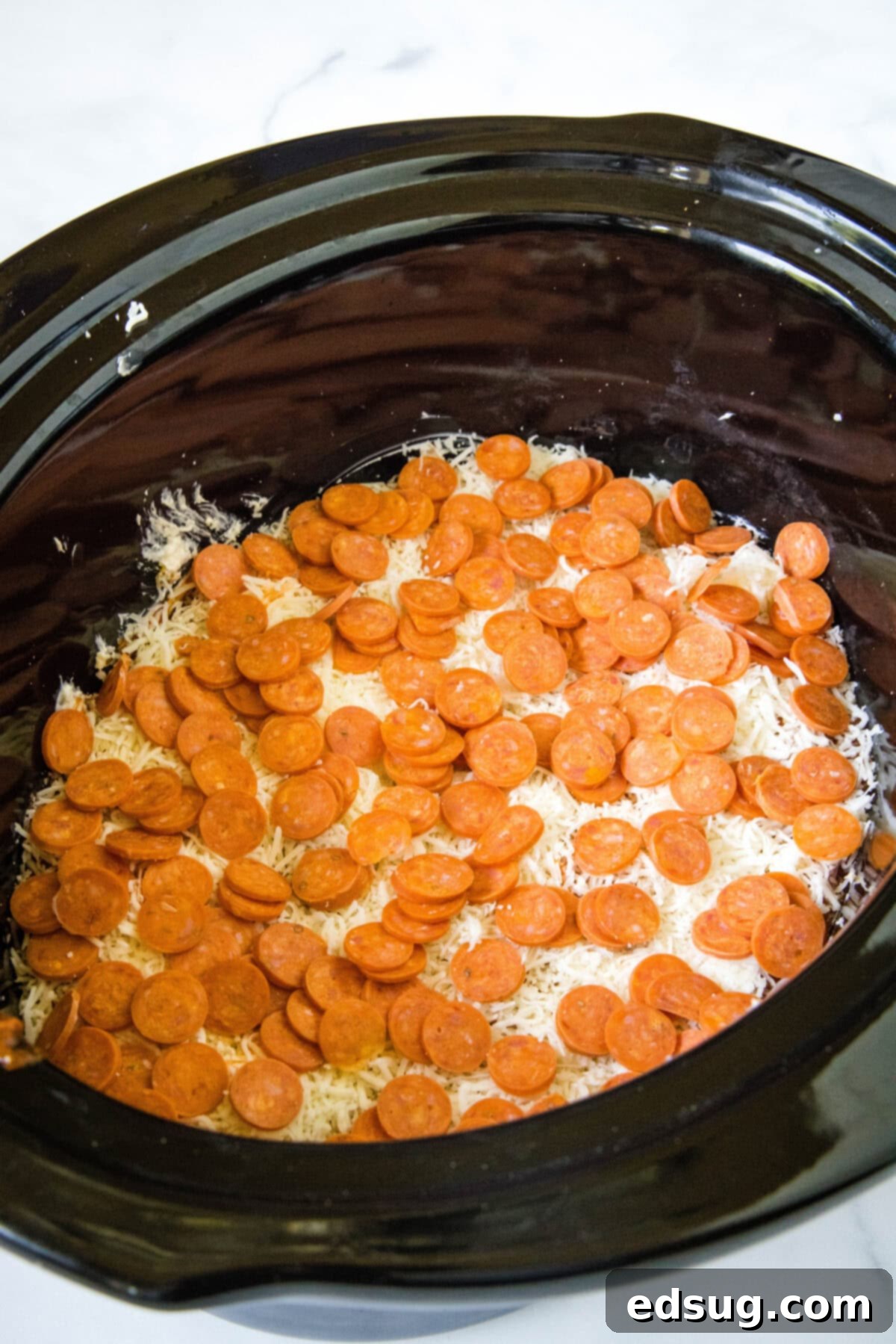 Layering pepperoni on top of the pizza dip in a slow cooker before cooking