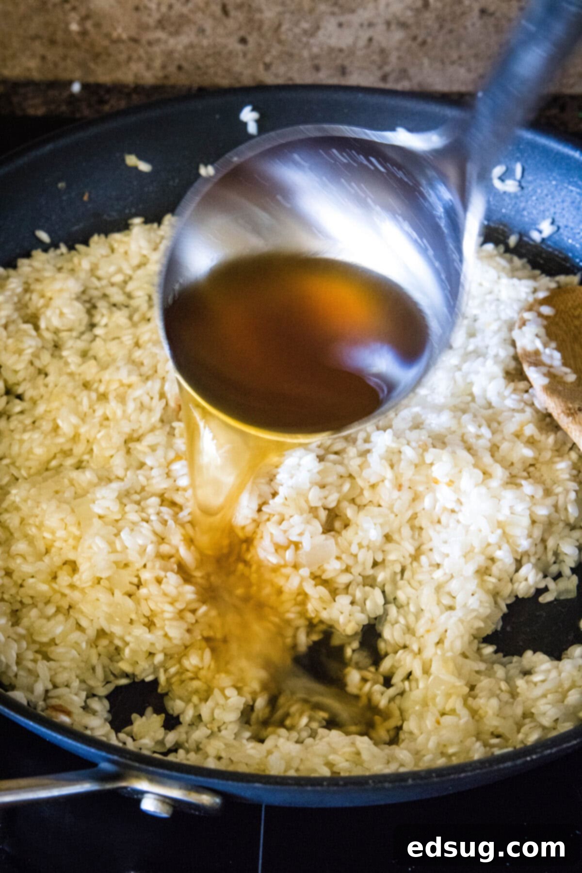 A ladle of broth being added to a skillet of simmering risotto.