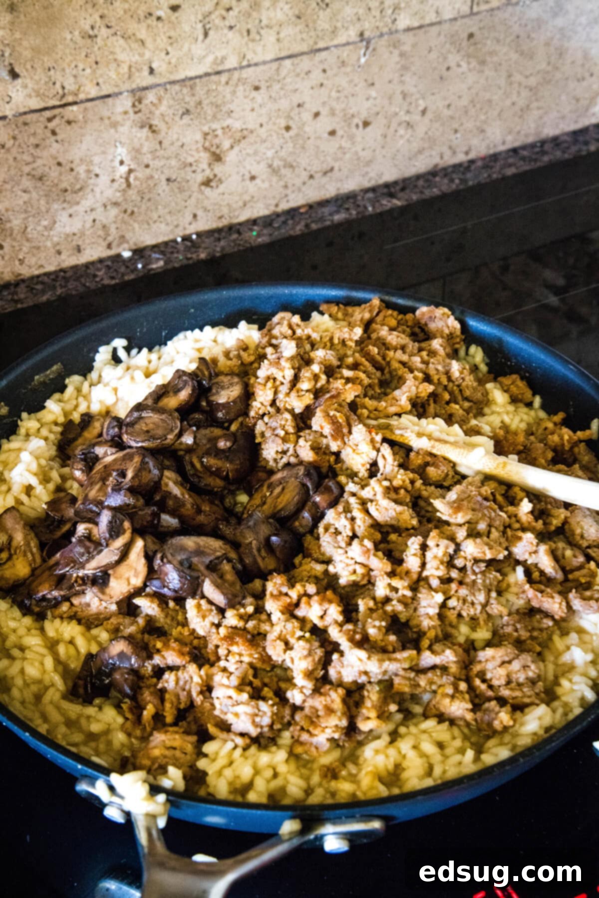 Browned sausage and mushrooms added to risotto in a skillet.