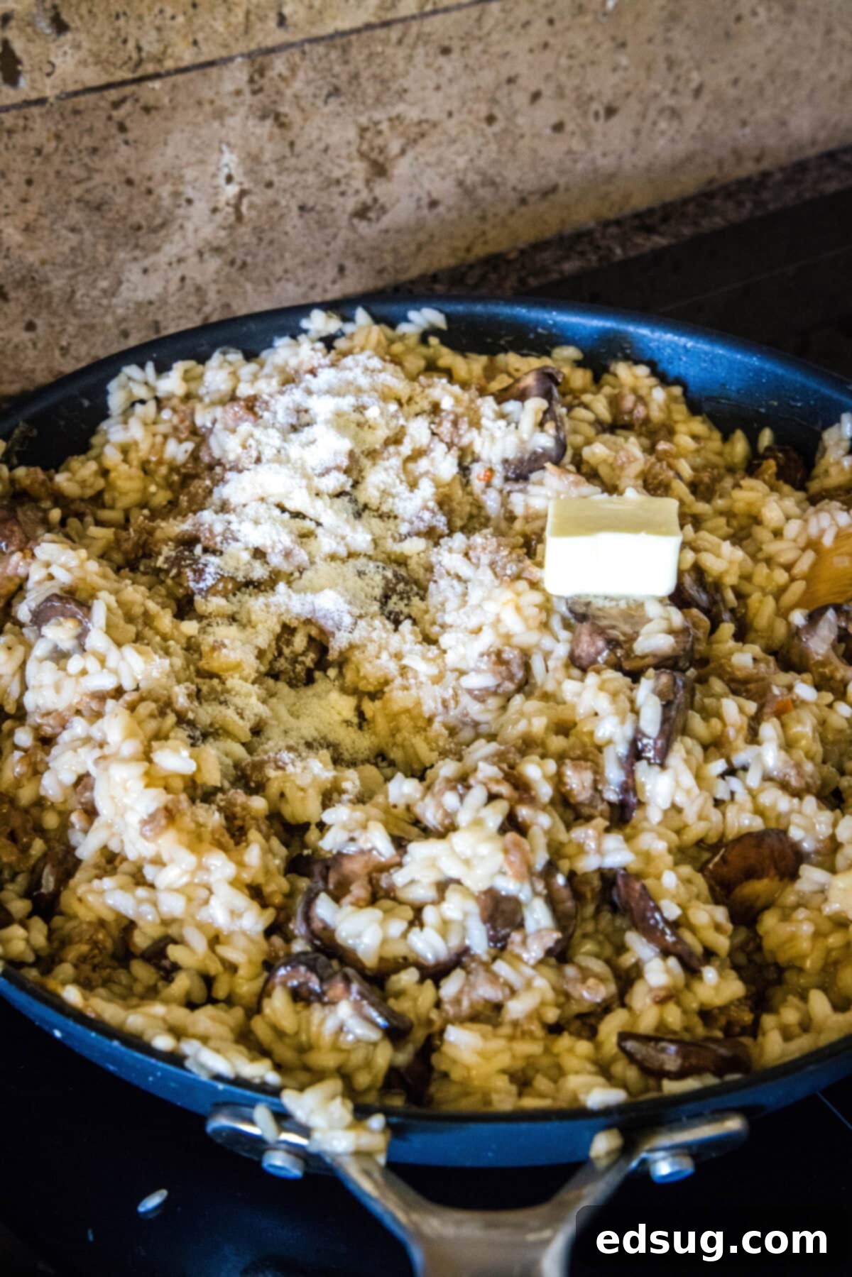 Butter and grated parmesan added to sausage risotto in a skillet.