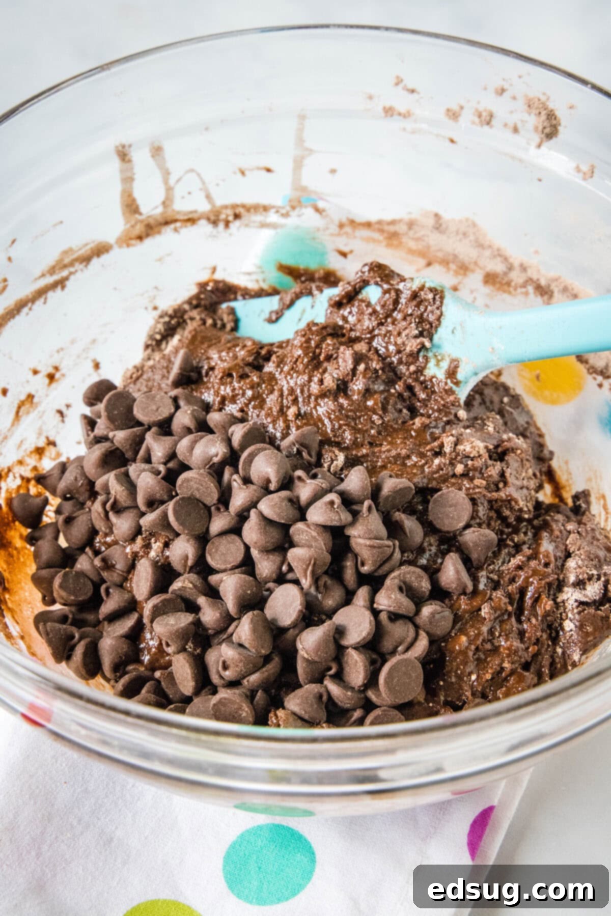 Brownie mix cookies are soft-baked, fudgy cookies made with only 4 ingredients! All you need is a box of brownie mix, oil, eggs, and flour. Close-up view of chocolate chips being folded into a rich, dark brownie cookie batter in a mixing bowl.