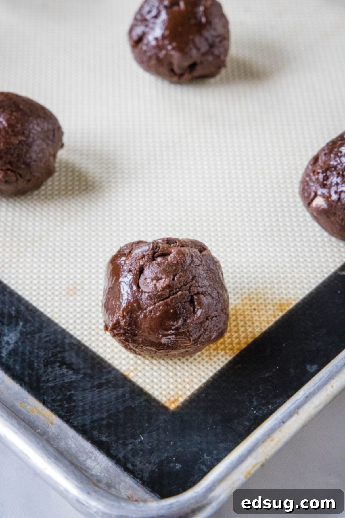 Brownie mix cookies are soft-baked, fudgy cookies made with only 4 ingredients! All you need is a box of brownie mix, oil, eggs, and flour. Rows of perfectly scooped brownie mix cookie dough balls, ready for baking, arranged on a baking sheet lined with parchment paper.
