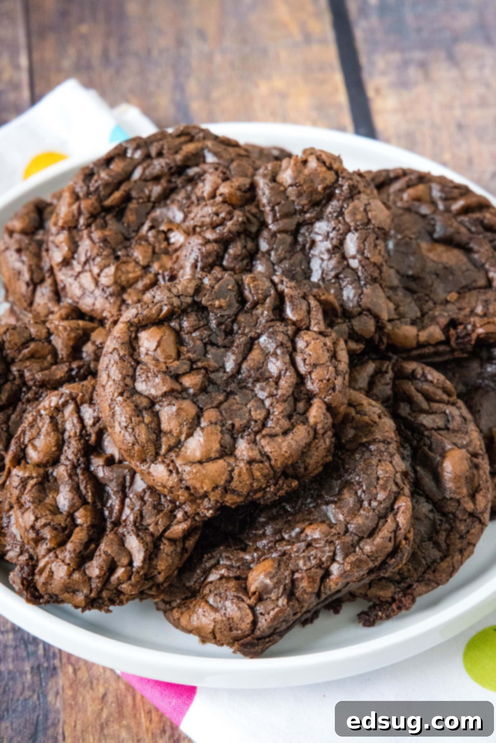 Brownie mix cookies are soft-baked, fudgy cookies made with only 4 ingredients! All you need is a box of brownie mix, oil, eggs, and flour. A generous pile of freshly baked brownie mix cookies, glistening with melted chocolate, arranged artfully on a white serving plate.