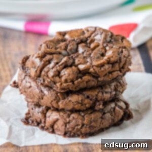 Fudgy Brownie Cookies 2 A stack of three brownie mix cookies on a piece of parchment paper.