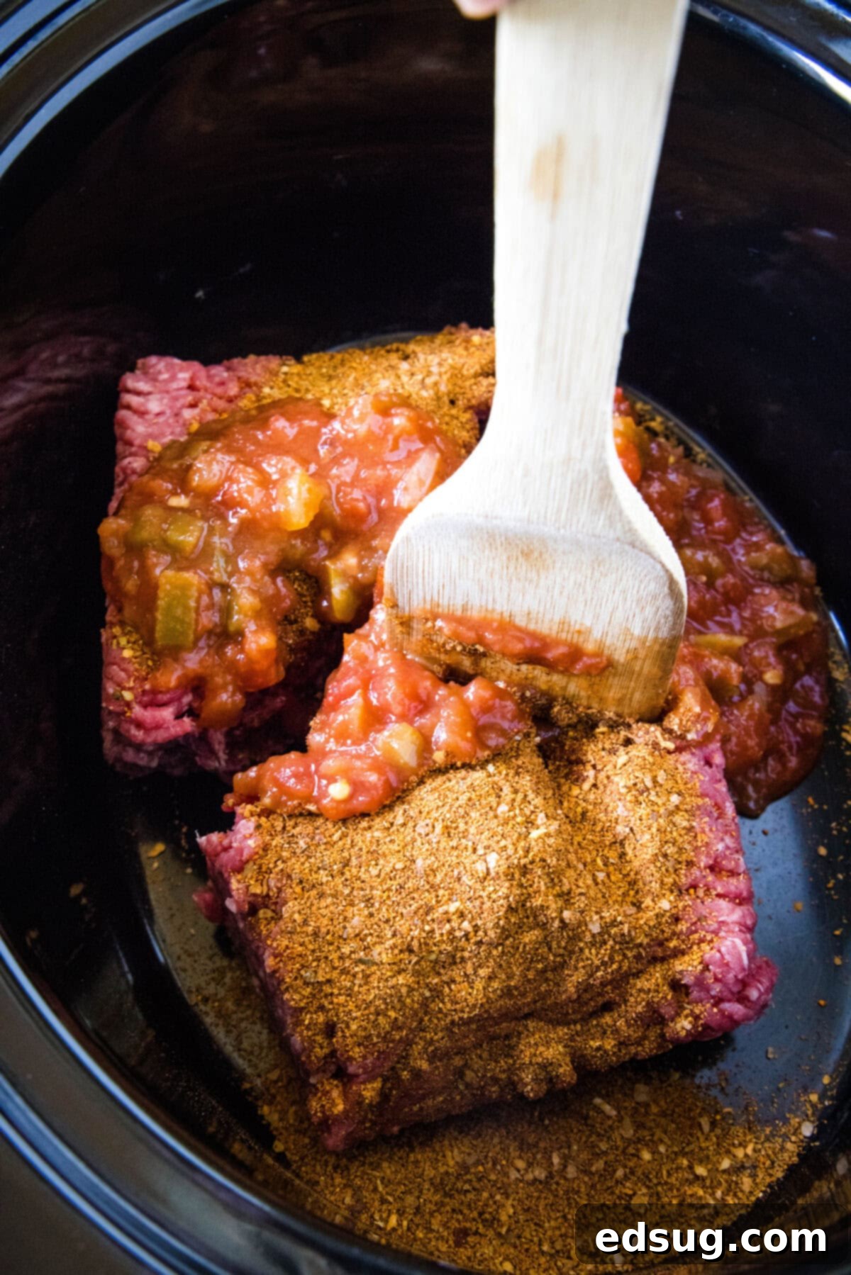 This slow cooker taco meat is an easy, 3-ingredient crock pot recipe that's packed with flavor. Perfect for parties and busy weeknights! A spatula is used to break up the ground beef inside the slow cooker, preparing it for seasoning.