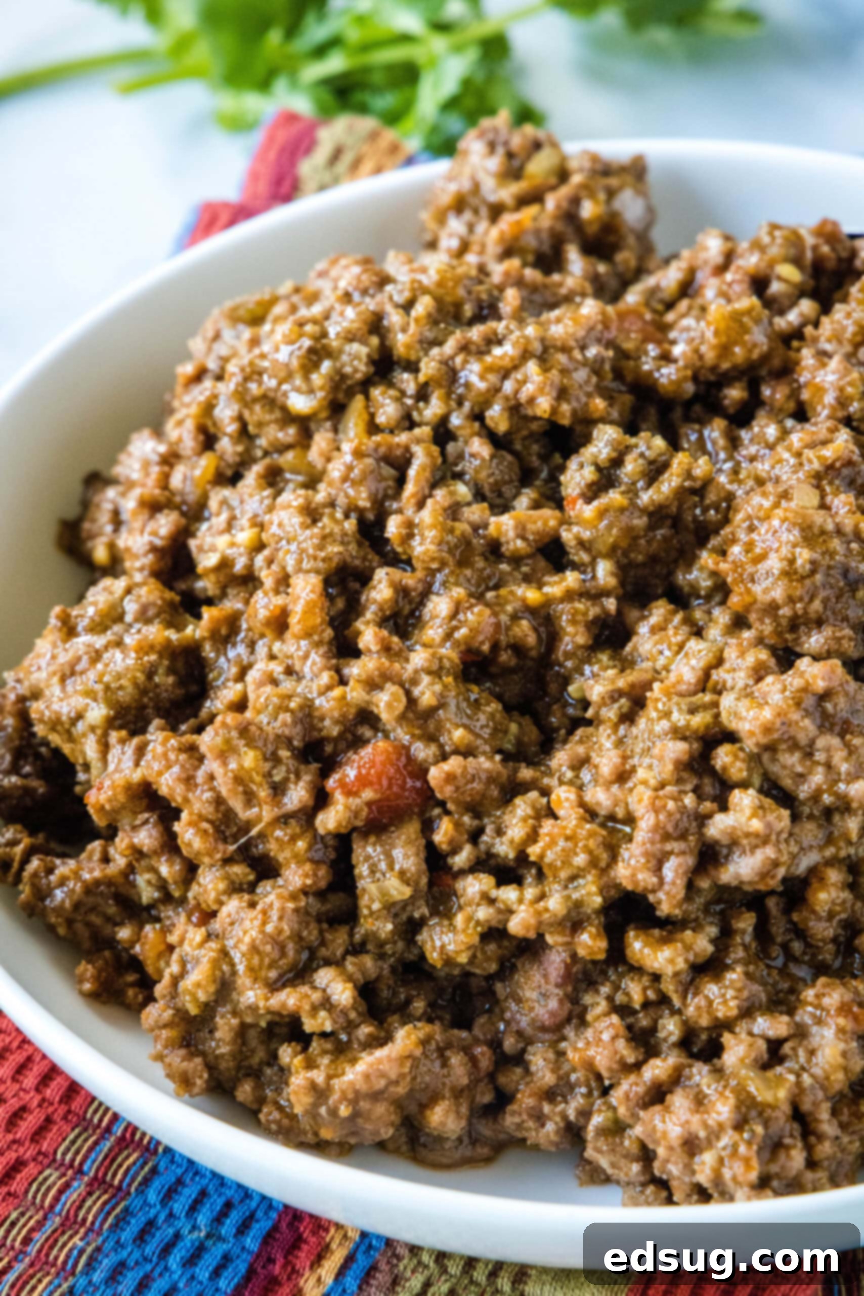 Note that while it’s fine to put raw meat in the slow cooker, you should never add frozen meat to the slow cooker before it’s thawed. Frozen meat stays at an unsafe temperature for too long in the low heat, risking the growth of bacteria. If you have frozen ground beef, be sure to thaw it completely before you use it. Generous serving of slow cooker taco meat in a large white bowl, garnished and ready for assembly.