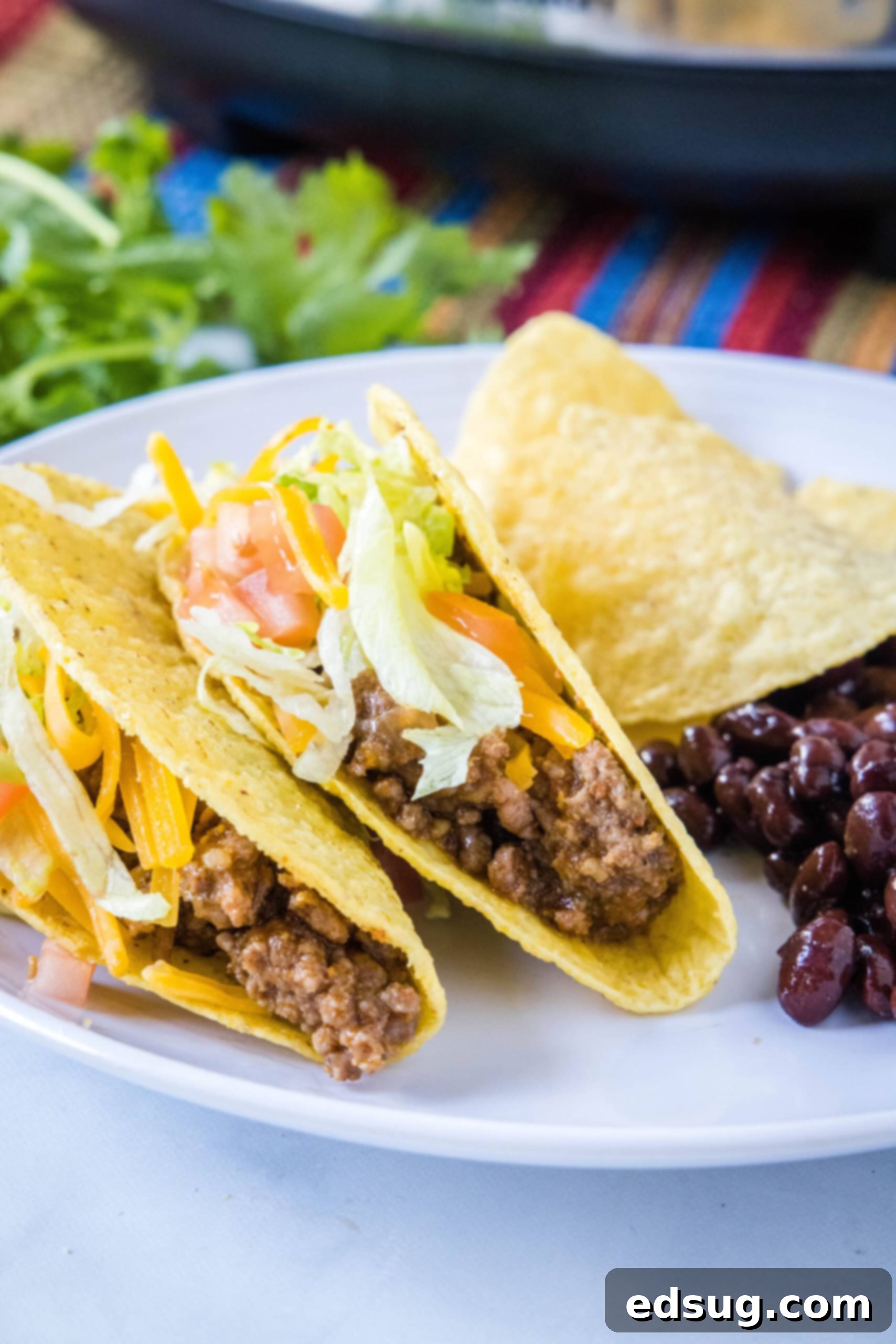This slow cooker taco meat is an easy, 3-ingredient crock pot recipe that's packed with flavor. Perfect for parties and busy weeknights! Two tacos filled with ground beef, alongside a scoop of black beans, on a white plate.