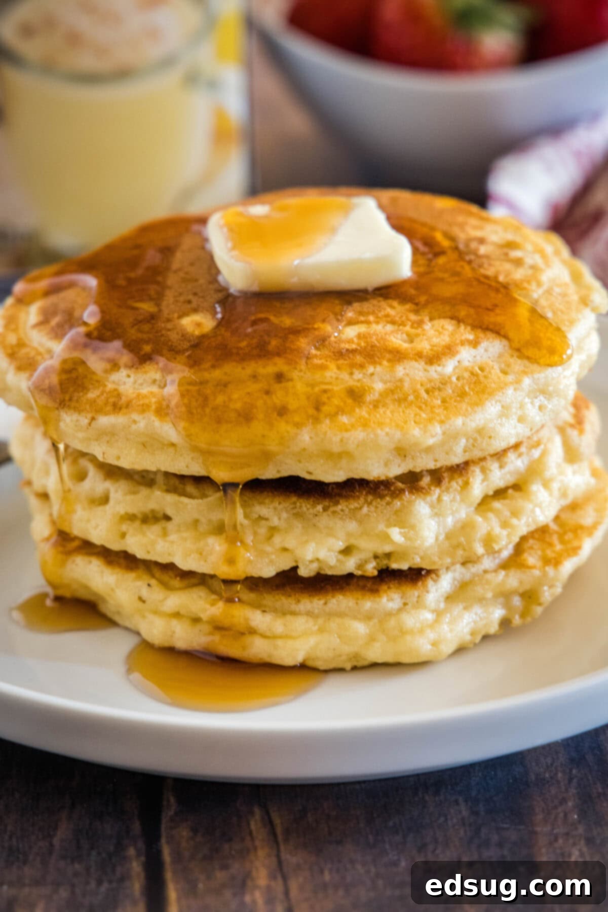 Creamy Spiced Eggnog Pancakes 2 A stack of golden, thick eggnog pancakes drizzled with maple syrup and topped with a pat of butter, resting on a crisp white plate, ready for a festive holiday breakfast.