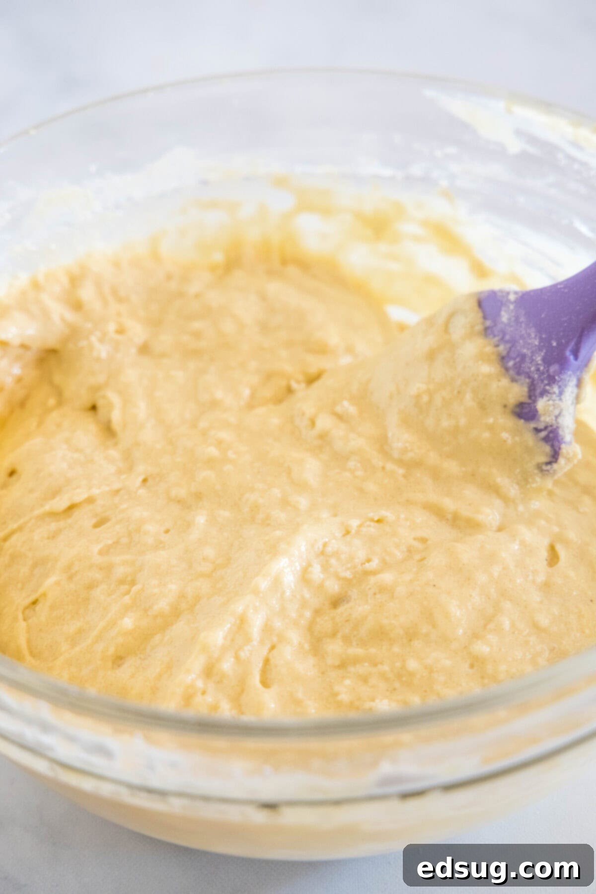 Creamy Spiced Eggnog Pancakes 4 A bowl filled with thick, golden eggnog pancake batter, ready to be cooked, with a whisk resting beside it.