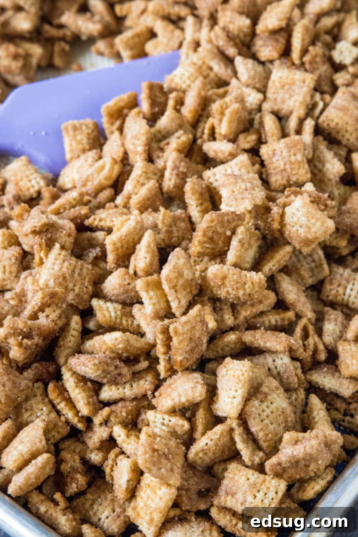 Churro Cinnamon Crunch 4 churro chex mix on a baking sheet being stirred with a spatula during baking