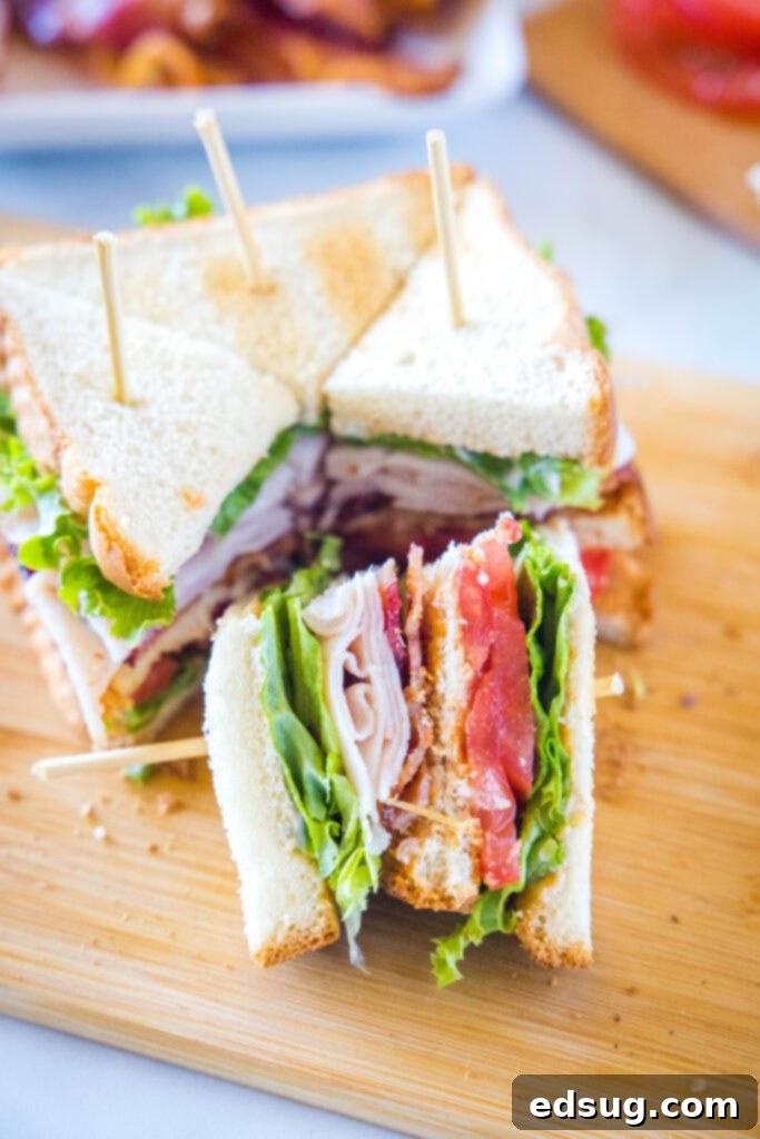 Ultimate Turkey Club Sandwich 4 turkey club sandwich sliced into quarters on a cutting board
