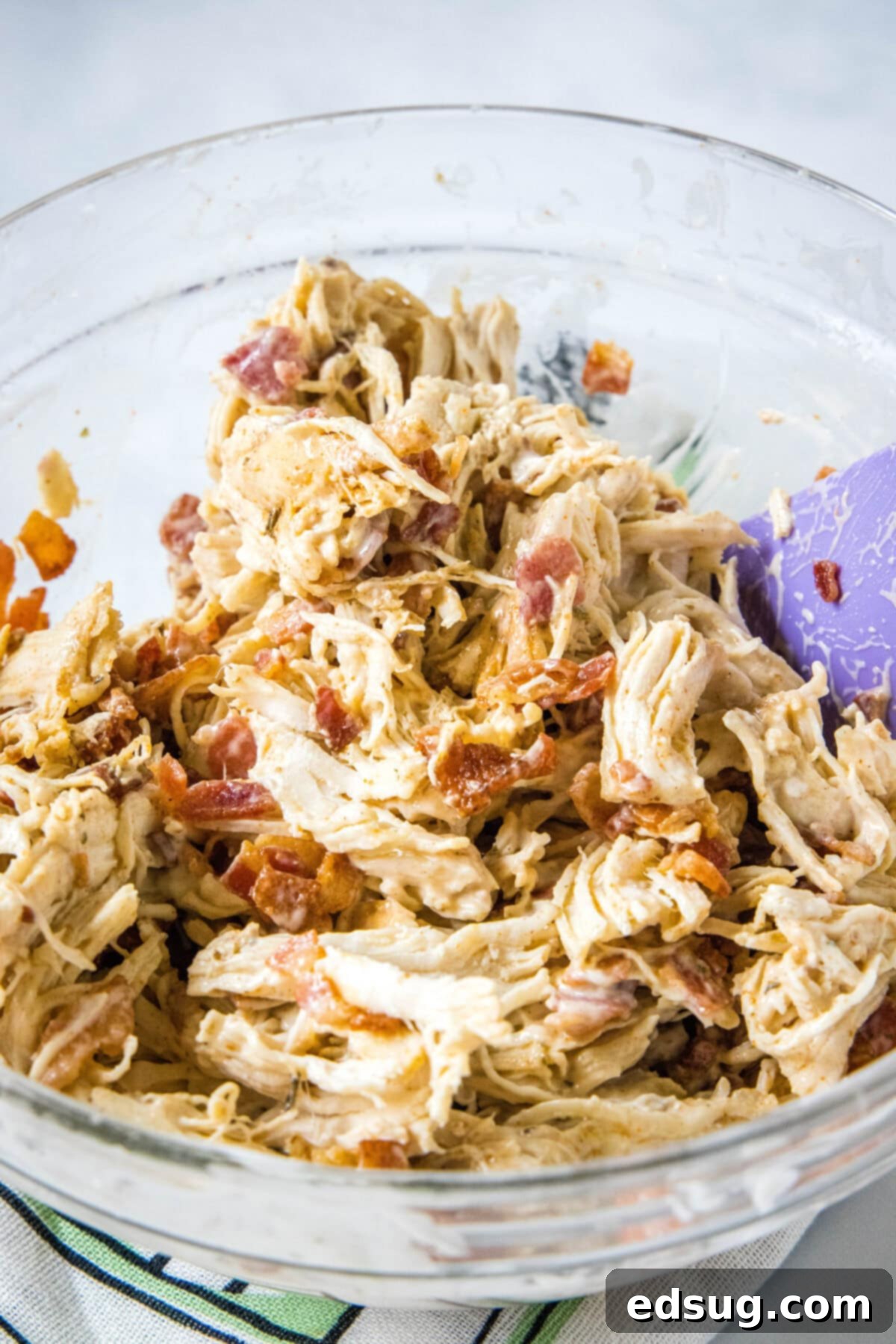 Make my easy chicken bacon ranch sliders with juicy shredded chicken, bacon, and creamy ranch dressing between sweet, fluffy Hawaiian rolls! Shredded chicken, bacon, and ranch mixture in a glass bowl.