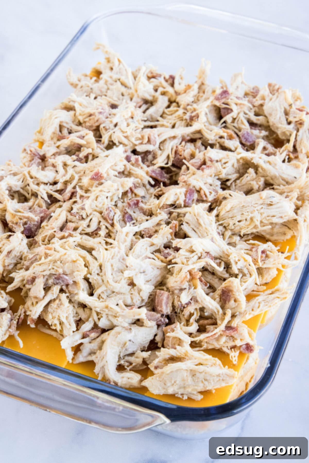 Make my easy chicken bacon ranch sliders with juicy shredded chicken, bacon, and creamy ranch dressing between sweet, fluffy Hawaiian rolls! Shredded ranch chicken and bacon layered over the bottom half of the Hawaiian rolls in a baking dish.