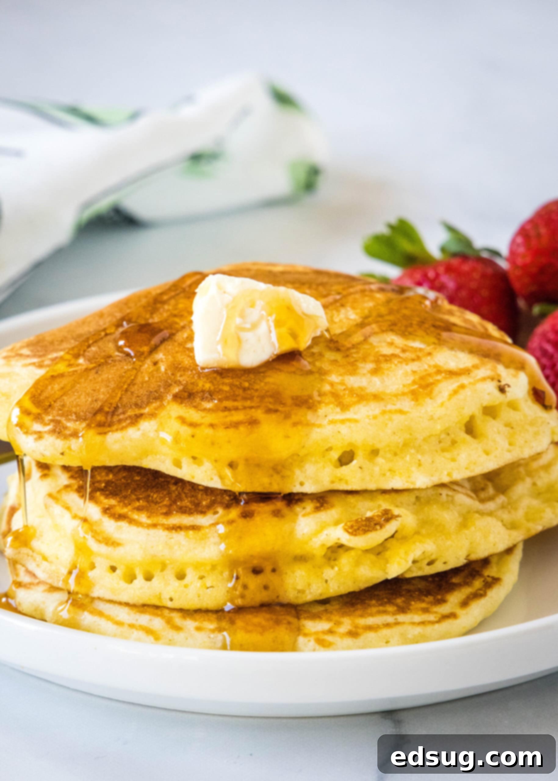 Experience the perfect blend of light and fluffy texture with these easy-to-make cornmeal pancakes, a delicious spin on traditional breakfast favorites. A tall stack of golden brown cornmeal pancakes, glistening with melted butter and drizzled with amber maple syrup, resting on a pristine white plate.