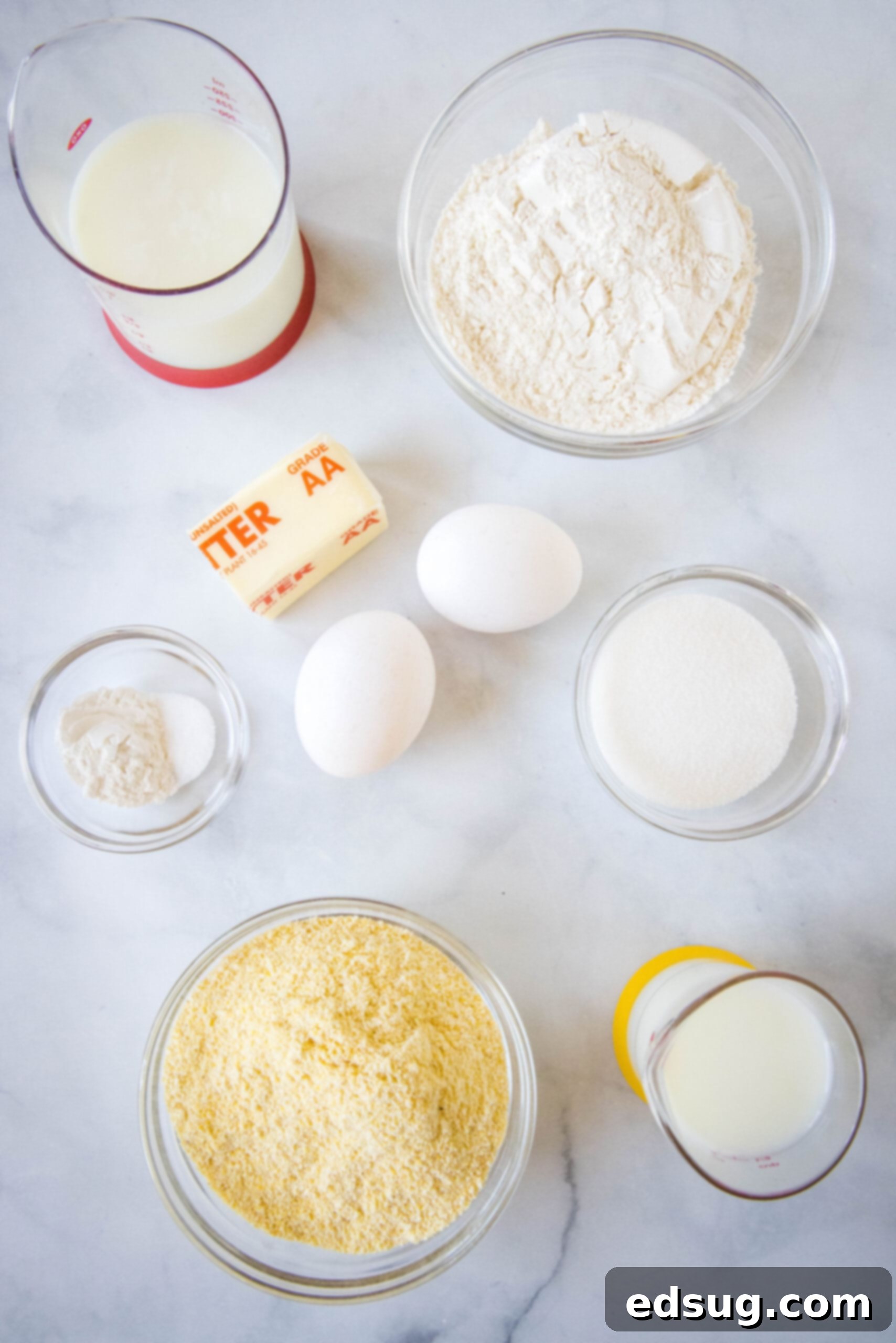 Discover the simple, wholesome ingredients needed to create perfectly light and fluffy cornmeal pancakes from scratch. A collection of fresh ingredients for cornmeal pancakes, including cornmeal, flour, eggs, buttermilk, and butter, neatly arranged on a white surface.