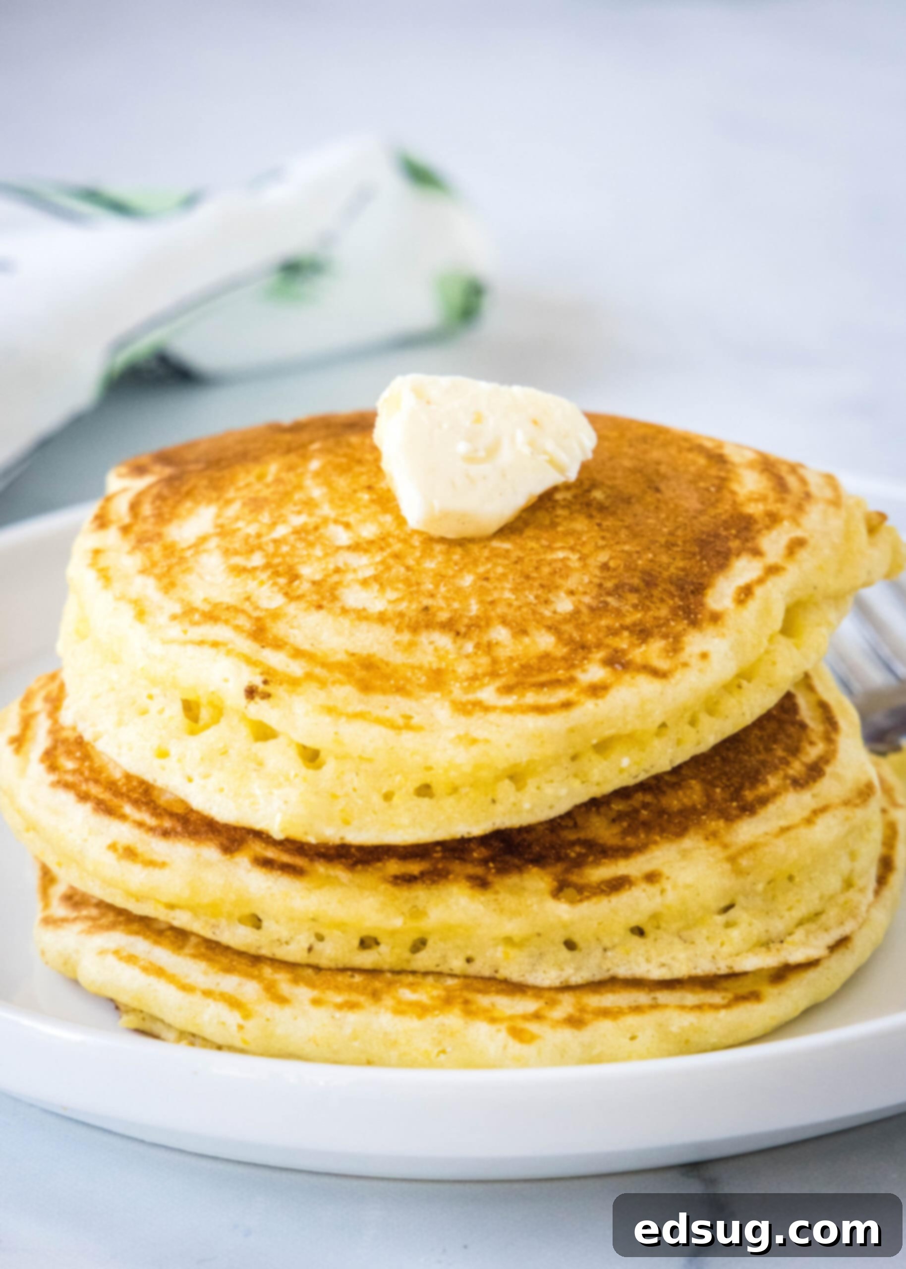 Enjoy these warm cornmeal pancakes topped with a simple pat of butter for a classic breakfast experience. A simple stack of freshly cooked cornmeal pancakes, adorned with a pat of melting butter, presented on a clean white plate.