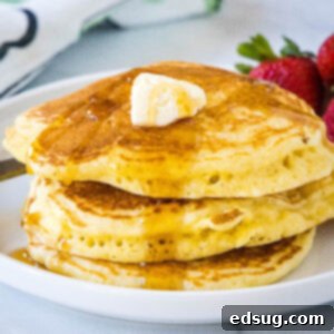 A stack of cornmeal pancakes topped with butter and maple syrup on a white plate.