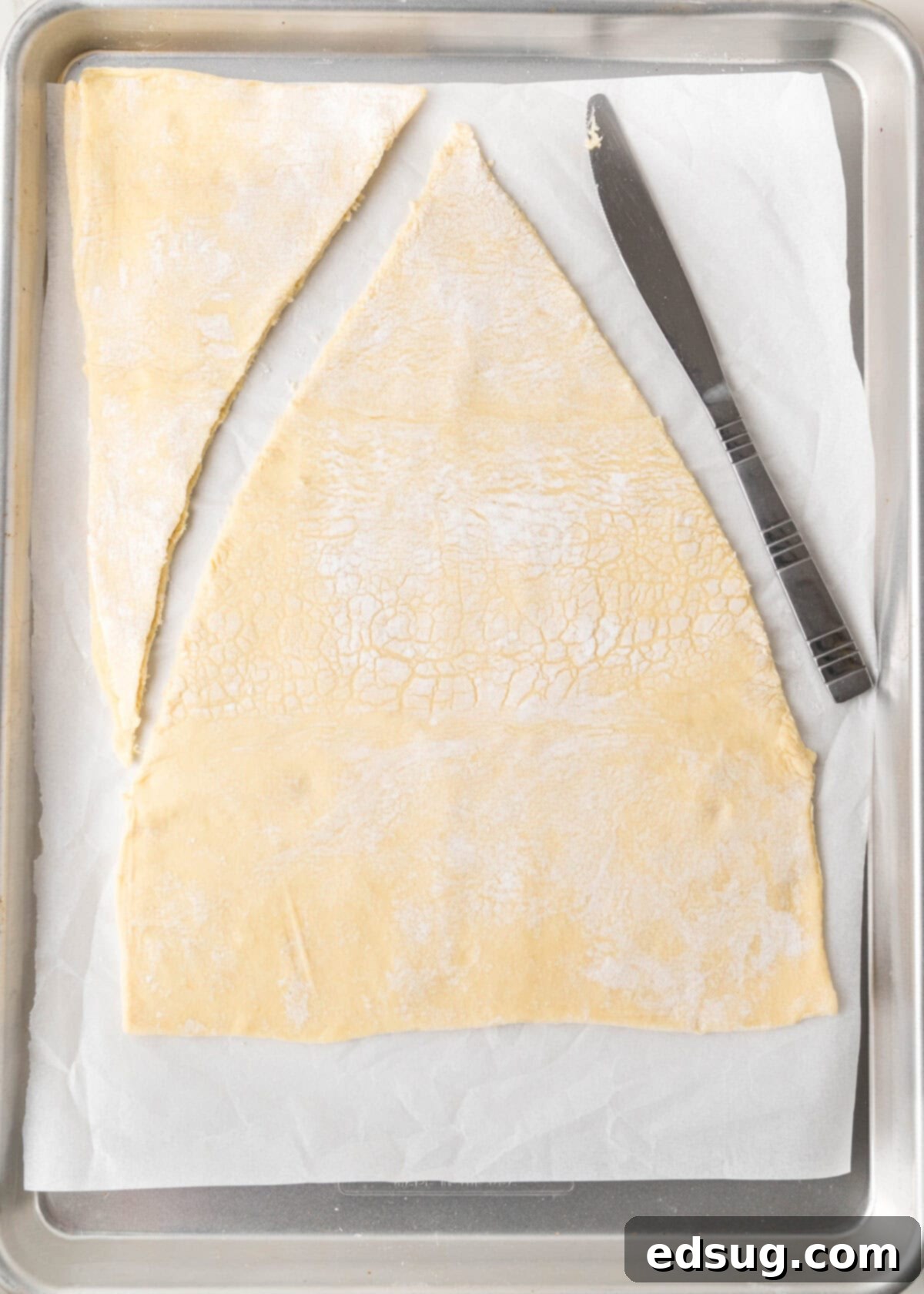 Holiday Swirl Pastry Tree 4 The initial stage of cutting puff pastry into the distinct shape of a Christmas tree on a baking sheet, preparing it for the filling.