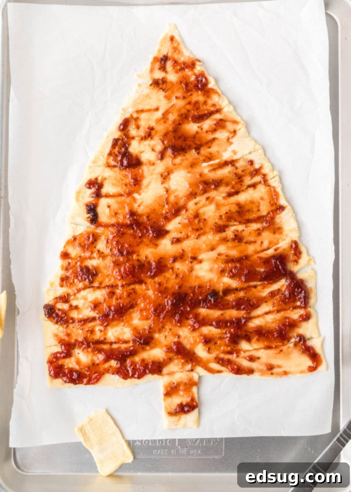 Holiday Swirl Pastry Tree 6 Strawberry jam being carefully spread over the bottom layer of puff pastry, preparing it for the top layer and twisting.
