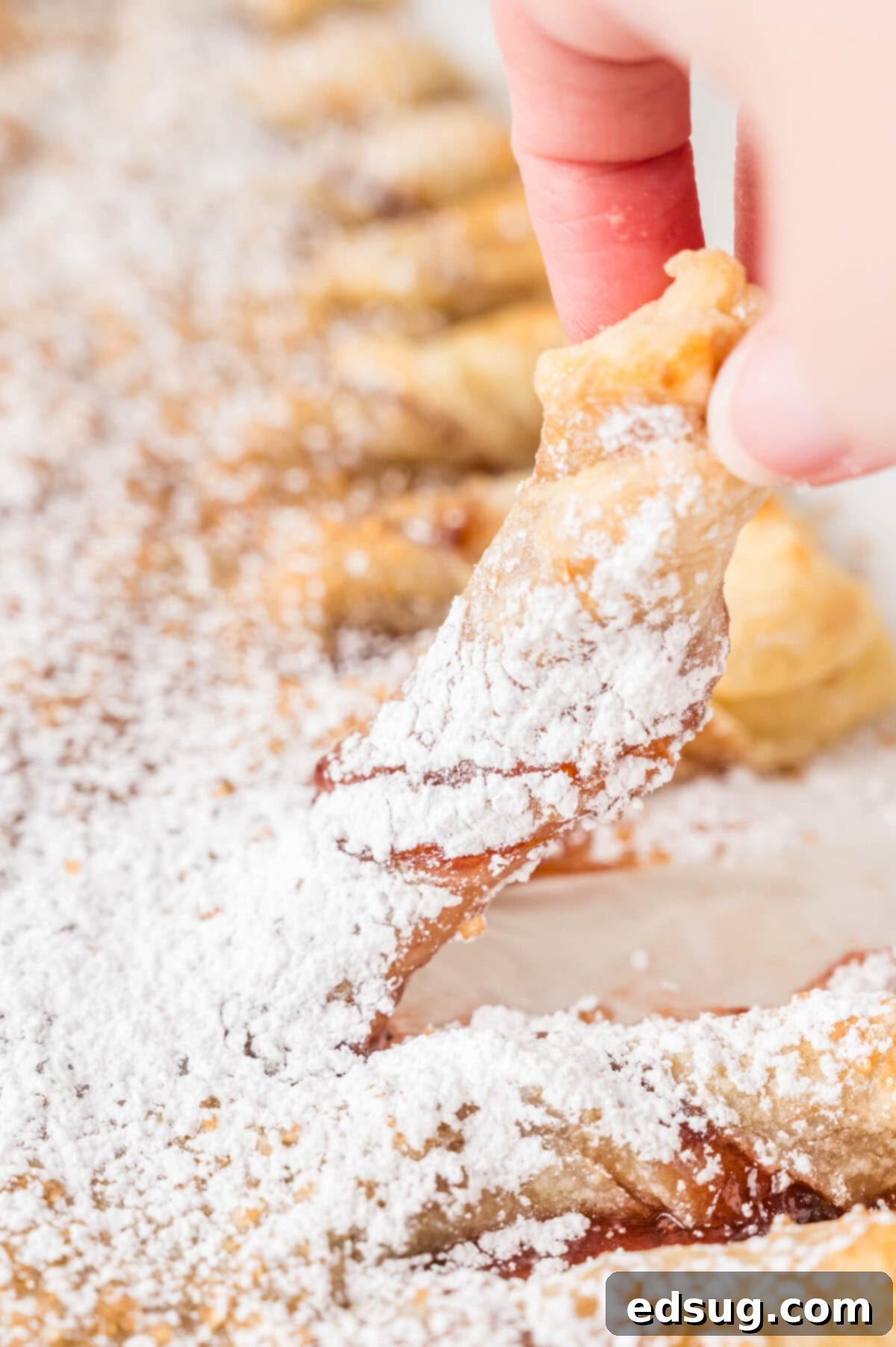 Holiday Swirl Pastry Tree 9 A hand gently taking a twisted branch off the freshly baked puff pastry Christmas tree, showing the delicious layers and filling.
