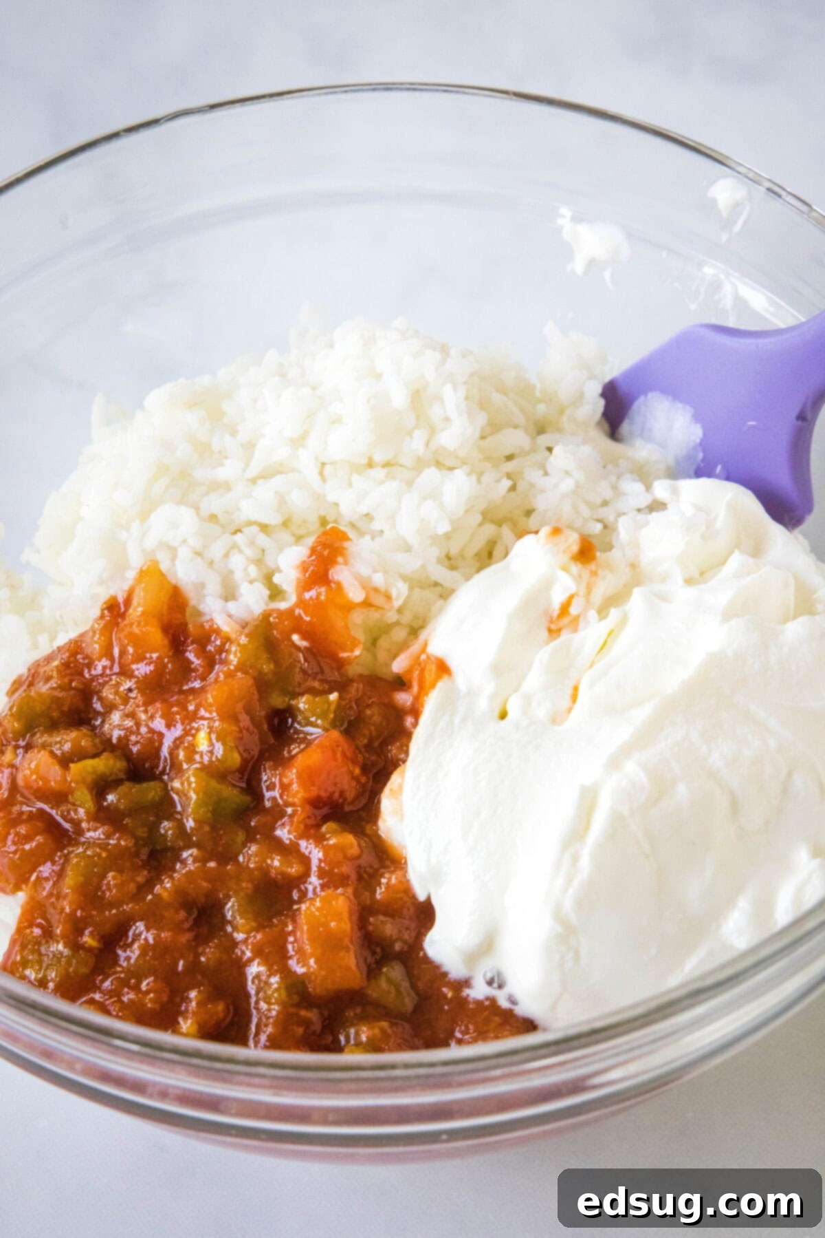 This chicken fajita casserole is an easy dinner packed with juicy chicken and rice, with sweet bell peppers, fajita seasoning, and cheese! Cooked white rice, sour cream, and salsa are combined in a clear glass mixing bowl, forming a creamy orange mixture.