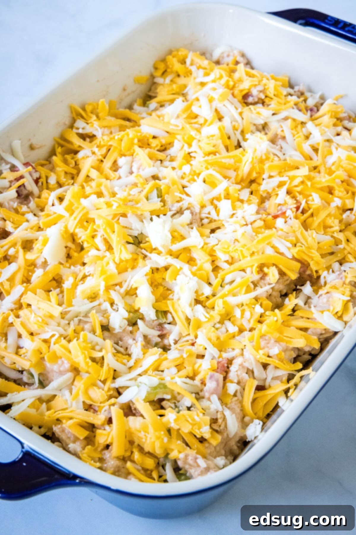 This chicken fajita casserole is an easy dinner packed with juicy chicken and rice, with sweet bell peppers, fajita seasoning, and cheese! The unbaked chicken fajita casserole filling in a baking dish, generously topped with shredded cheese, ready for the oven.