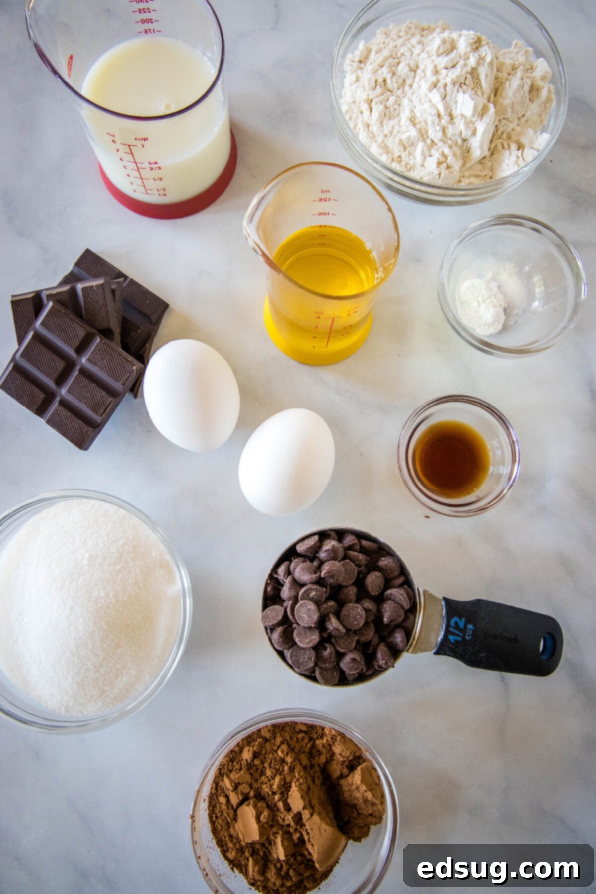 Fudgy Brownie Muffins 3 Brownie muffin ingredients laid out on a counter, including flour, cocoa powder, chocolate chips, eggs, milk, oil, and sugar.