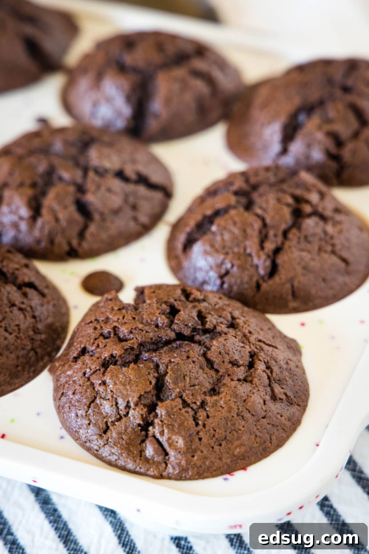 Fudgy Brownie Muffins 4 Freshly baked brownie muffins cooling in a muffin pan, showing their perfectly risen and cracked tops.