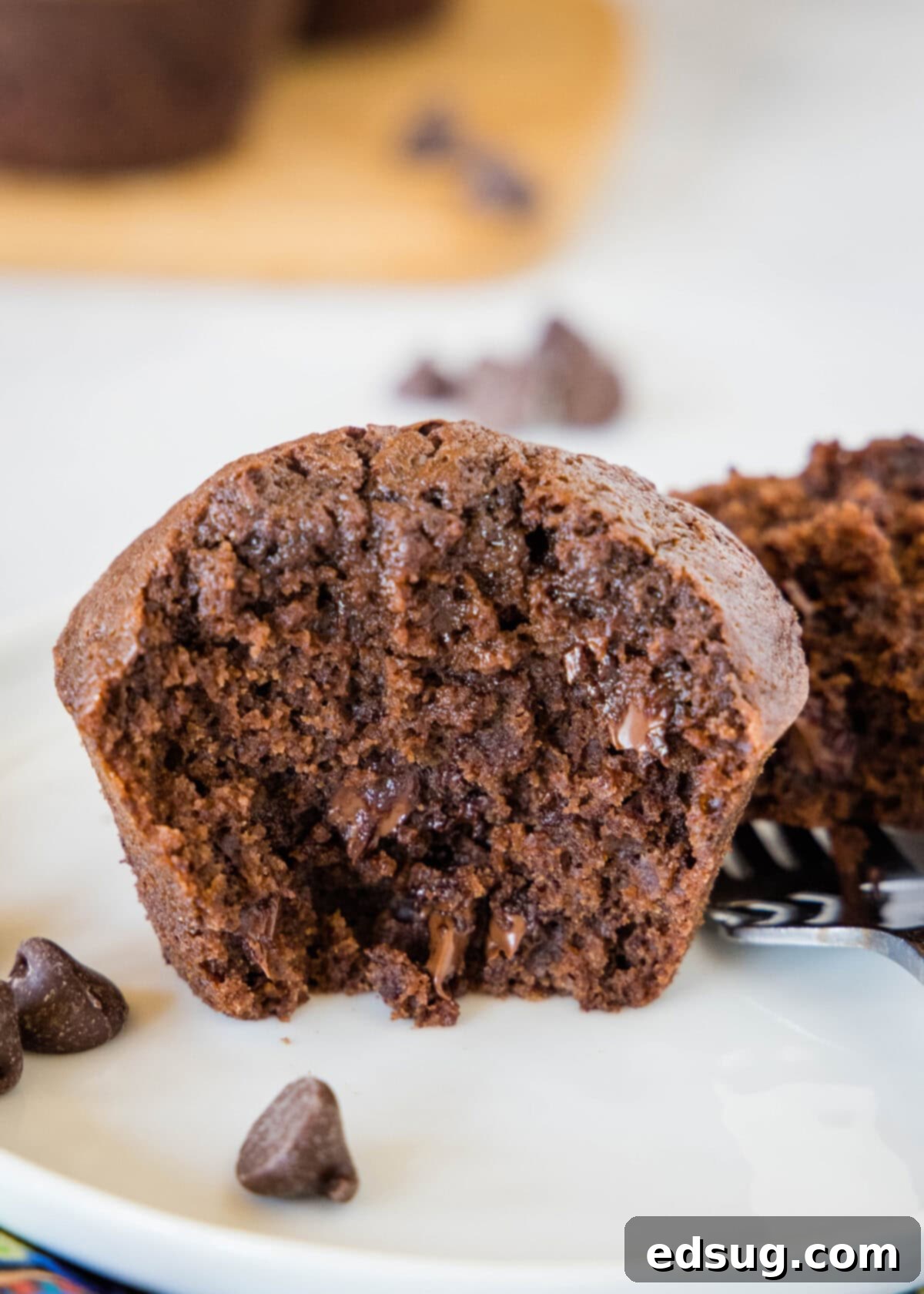 Fudgy Brownie Muffins 6 A fudgy brownie muffin cut in half, revealing its moist, dense interior and abundant melted chocolate chips, resting on a pristine white plate.