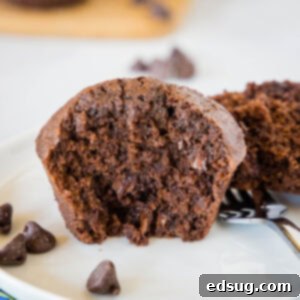 Close up of a brownie muffin cut in half on a white plate, showing its fudgy interior and melted chocolate chips.