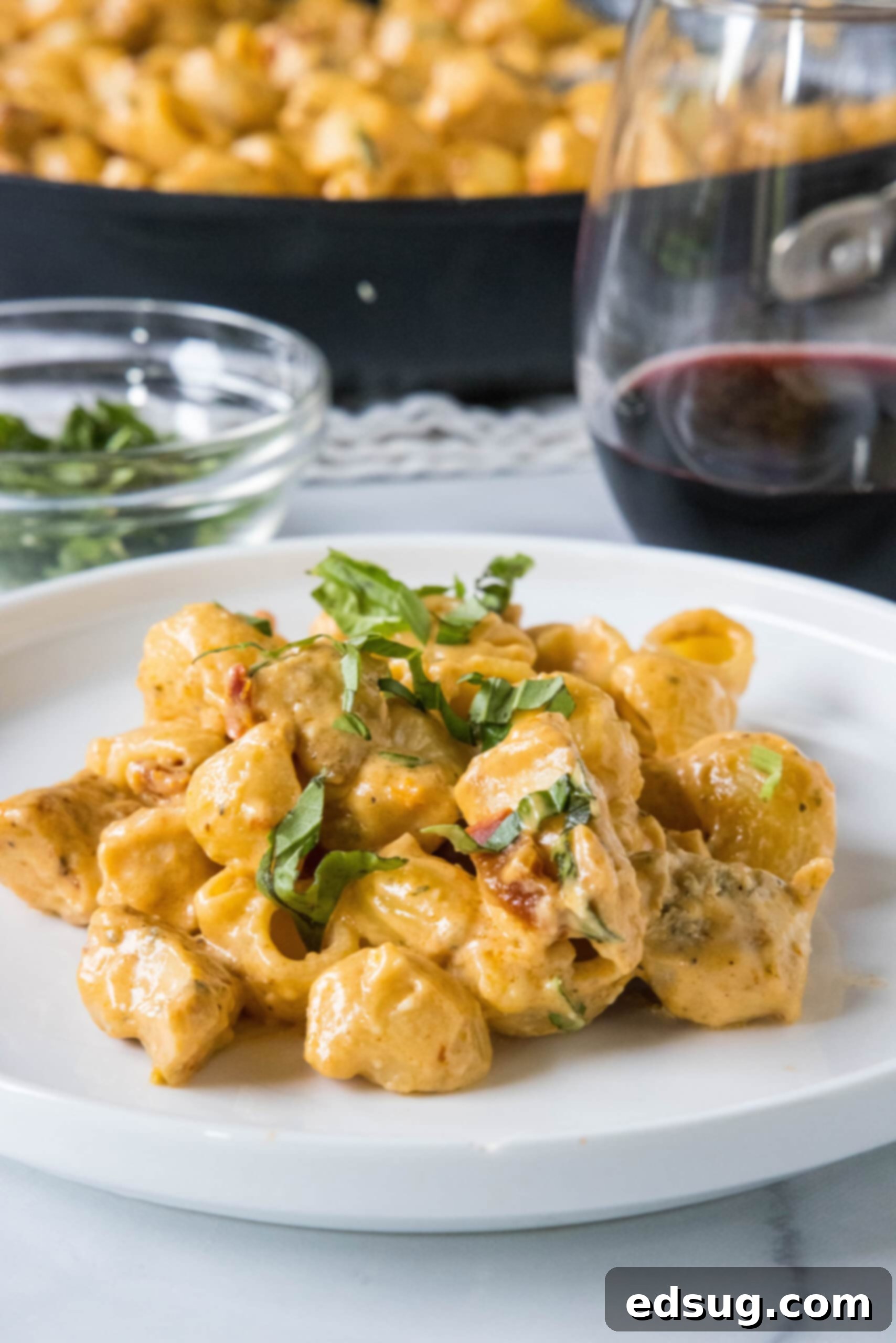 Flavor-packed Marry Me Chicken pasta is a 30-minute, one-pan weeknight dinner with tender pasta and chicken in creamy sun-dried tomato sauce. A serving of Marry Me Chicken pasta on a white plate, with the rest of the pasta in a skillet in the background.