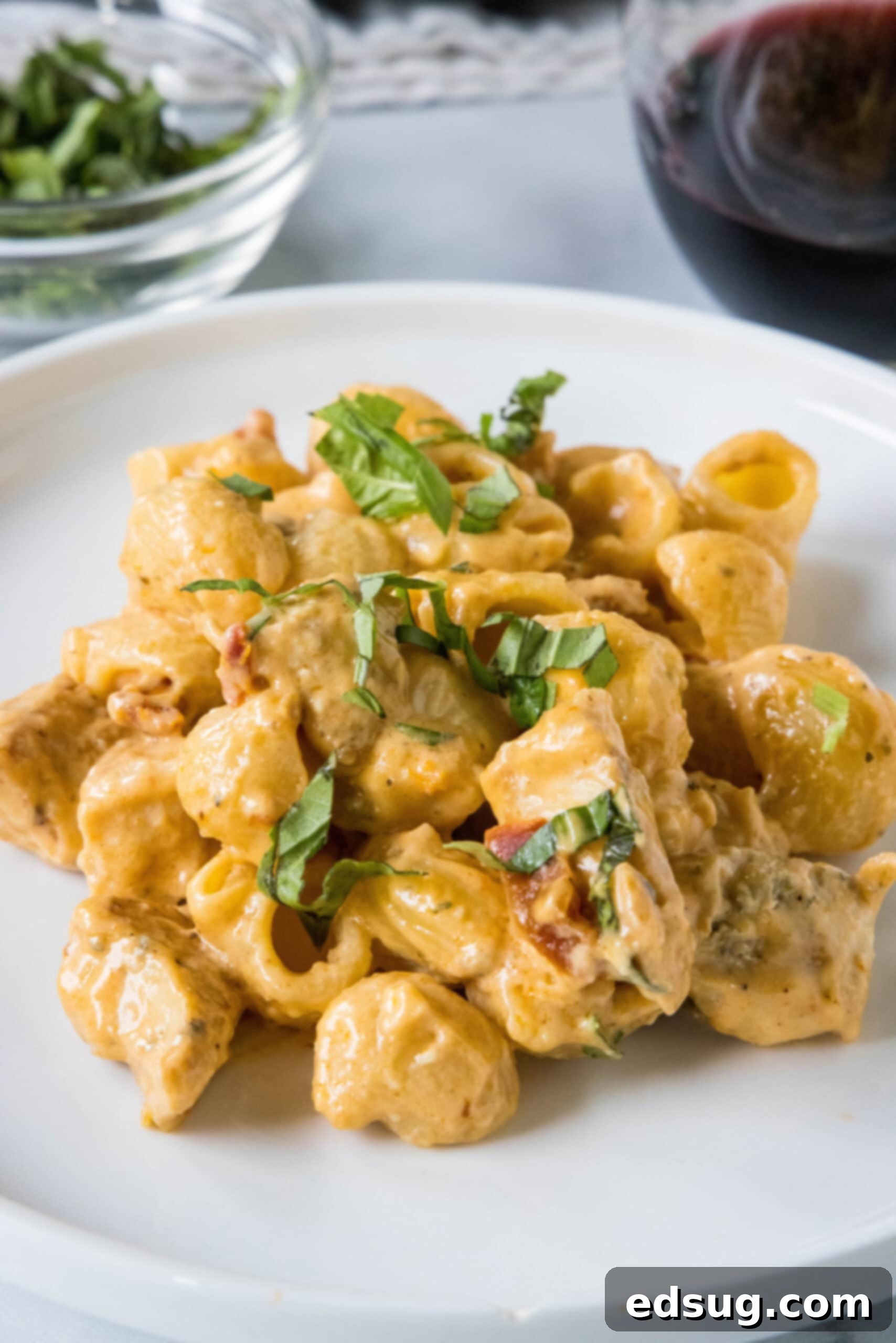 Flavor-packed Marry Me Chicken pasta is a 30-minute, one-pan weeknight dinner with tender pasta and chicken in creamy sun-dried tomato sauce. A serving of Marry Me Chicken pasta on a white plate, with the rest of the pasta in a skillet in the background.