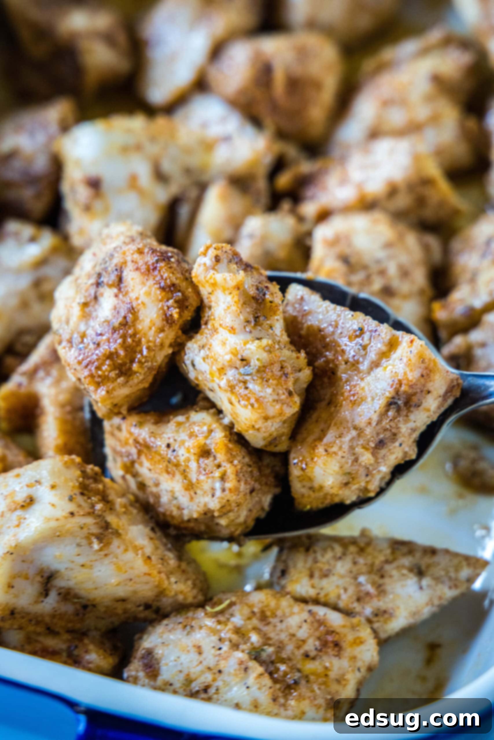A serving spoon scooping baked chicken bites from a ceramic baking dish. A serving spoon lifting juicy, golden baked chicken bites from a ceramic baking dish, ready to be served.