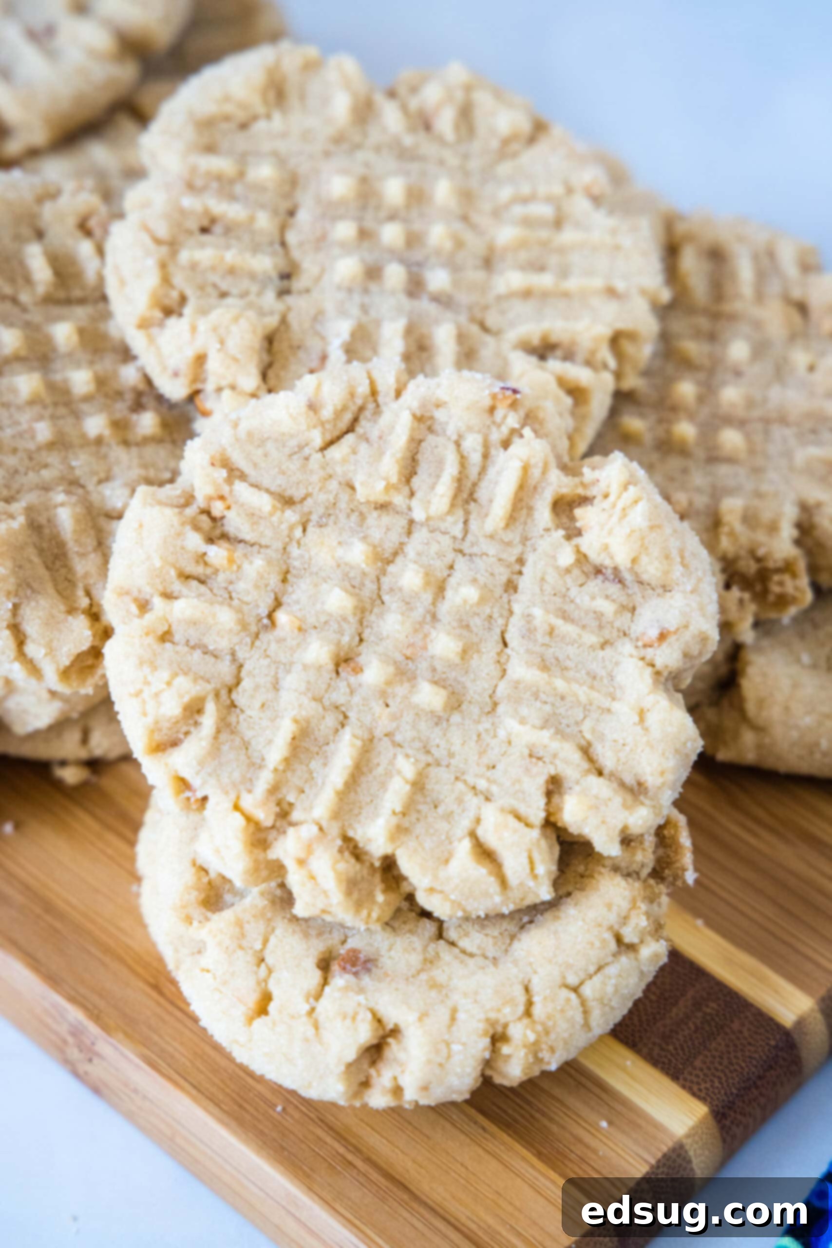 A generous pile of freshly baked, golden-brown crunchy peanut butter cookies, artfully arranged on a wooden cutting board, inviting a taste.