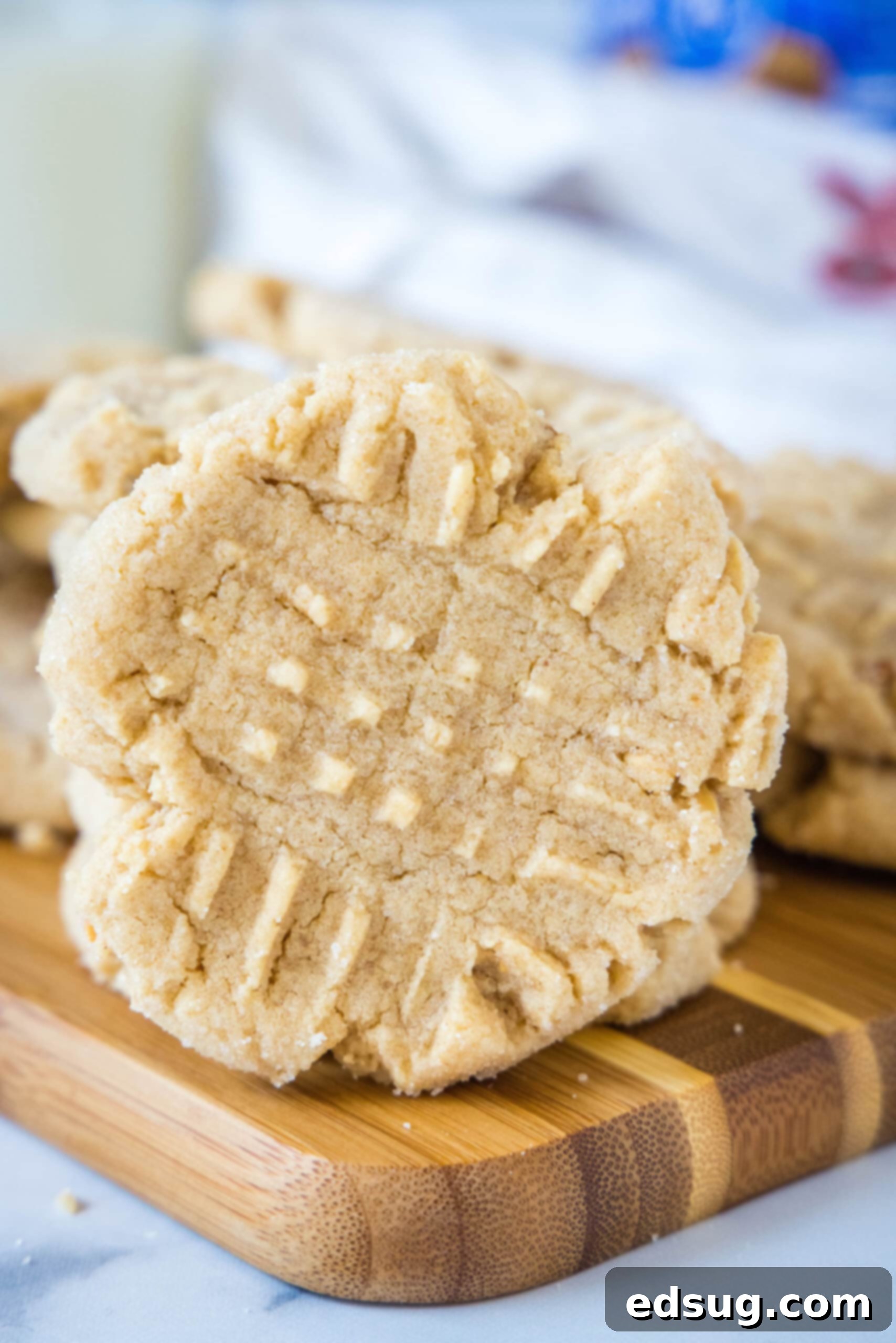 A single perfectly baked crunchy peanut butter cookie propped against a backdrop of more cookies on a wooden cutting board, highlighting its texture.