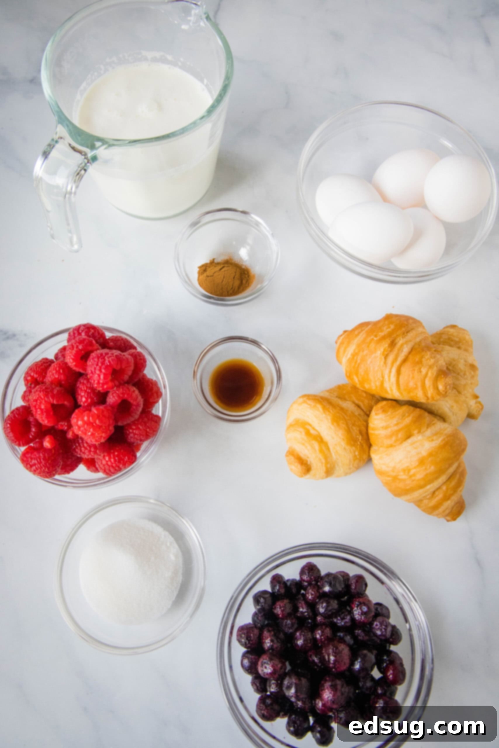 This overnight croissant baked French toast has buttery croissants layered in a rich, spiced custard with berries. It's prepped in minutes! Ingredients needed for croissant baked French toast, including eggs, milk, sugar, vanilla, cinnamon, and fresh berries.