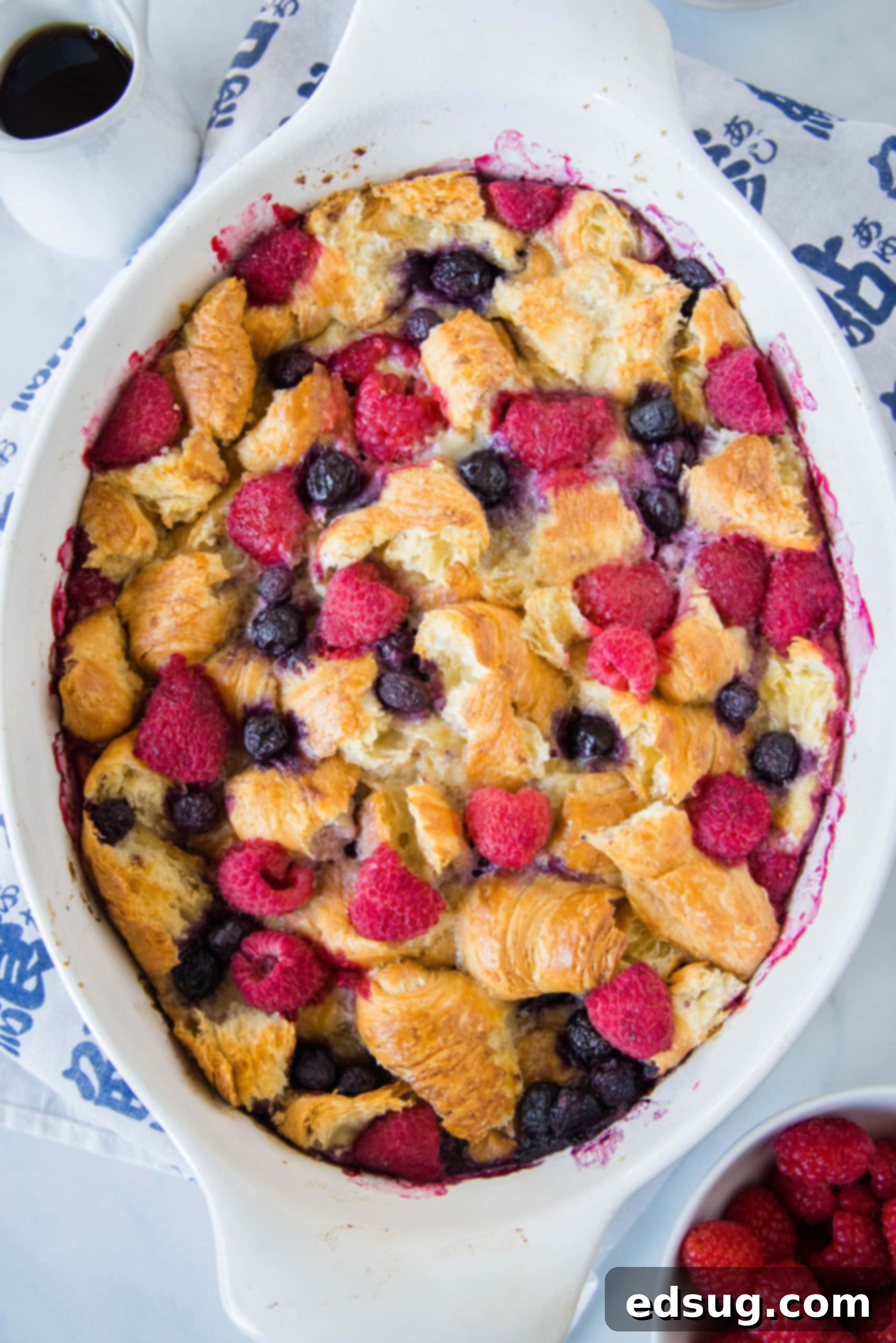 This overnight croissant baked French toast has buttery croissants layered in a rich, spiced custard with berries. It's prepped in minutes! Overhead view of a perfectly baked croissant French toast casserole in a large oval dish, golden and puffed.