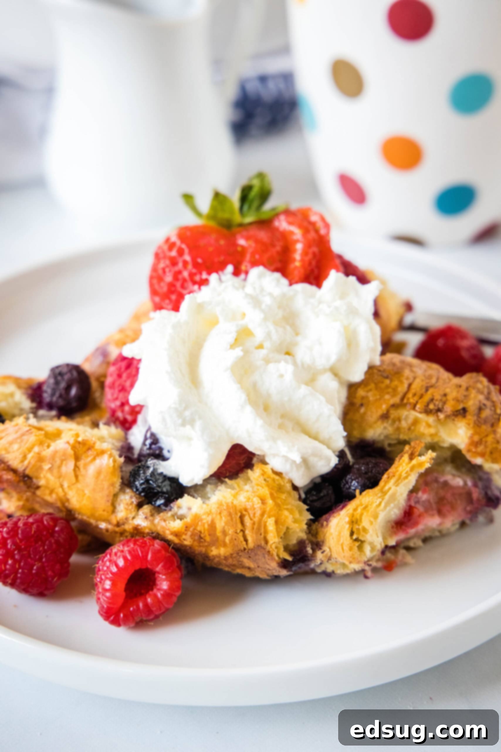 This overnight croissant baked French toast has buttery croissants layered in a rich, spiced custard with berries. It's prepped in minutes! A serving of croissant baked French toast on a plate, adorned with a swirl of whipped cream and a handful of fresh berries.
