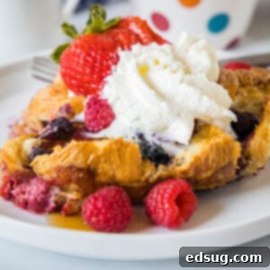 Decadent Croissant French Toast Bake 2 A serving of croissant baked French toast topped with maple syrup, whipped cream, and fresh berries on a plate.