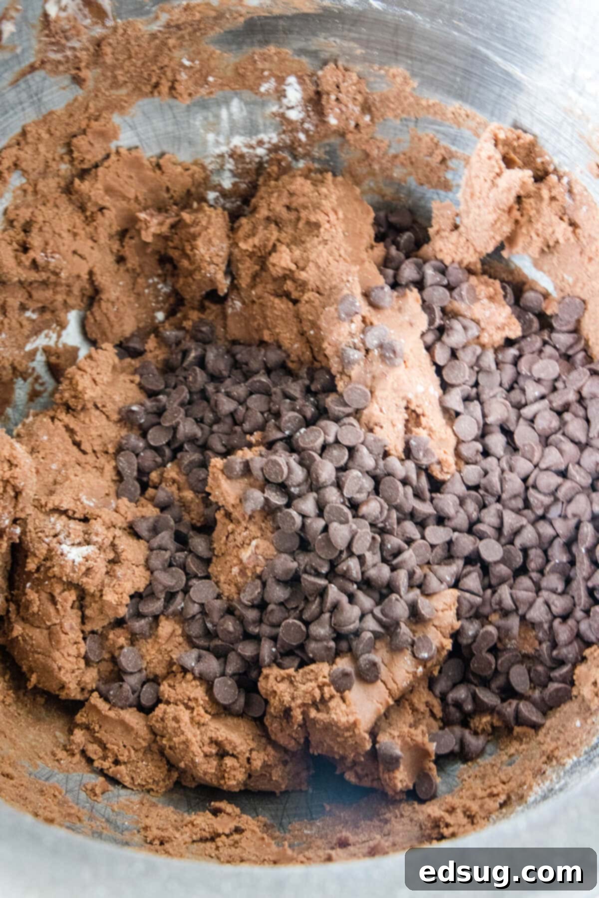 Chocolate snowball cookies are a fun twist on Mexican wedding cookies! These soft chocolate cookies are quick to make and irresistibly fudgy. Chocolate chips being folded into a rich, dark chocolate cookie dough in a mixing bowl.