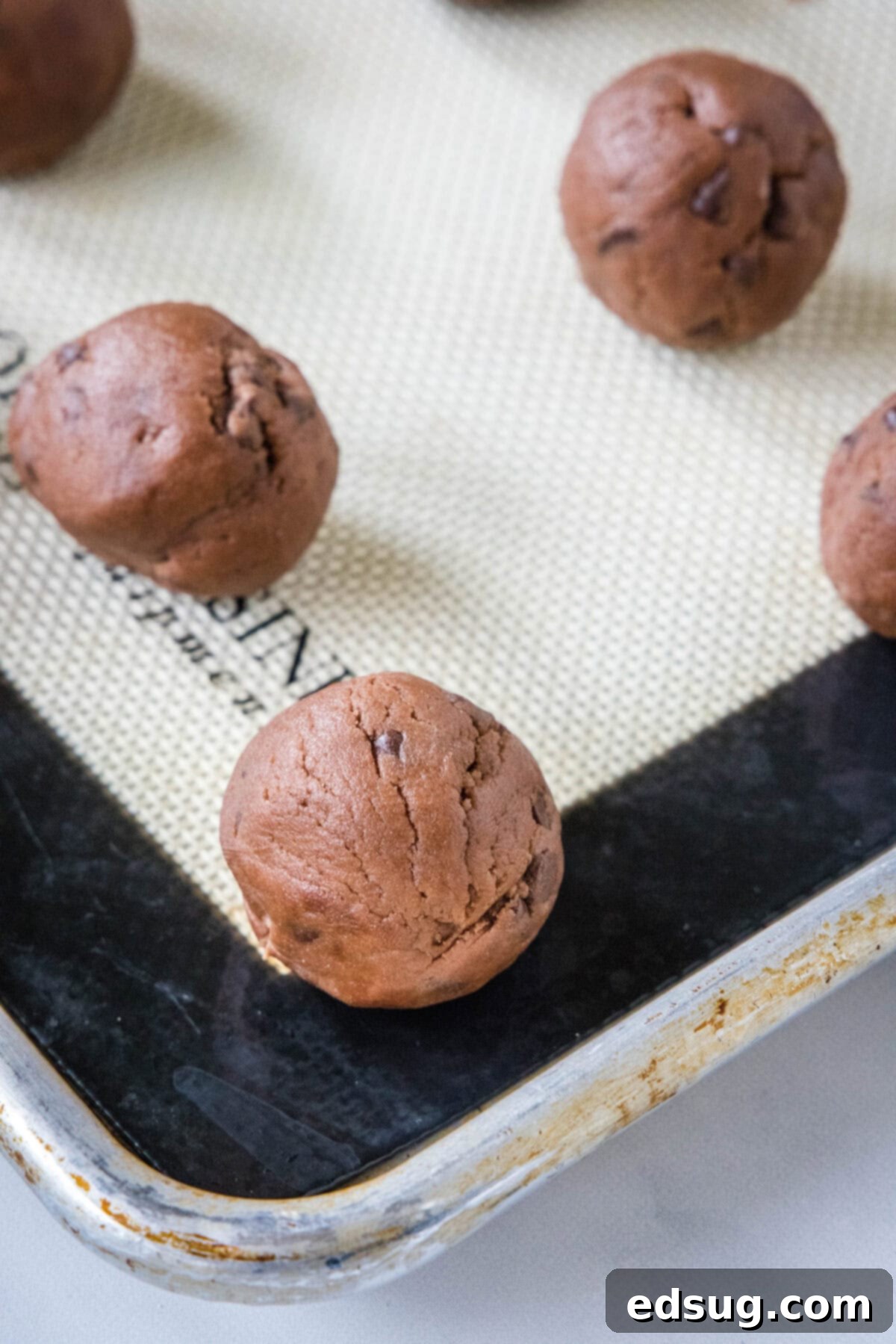 Chocolate snowball cookies are a fun twist on Mexican wedding cookies! These soft chocolate cookies are quick to make and irresistibly fudgy. Neatly rolled chocolate cookie dough balls arranged on a silpat-lined baking sheet, ready for the oven.