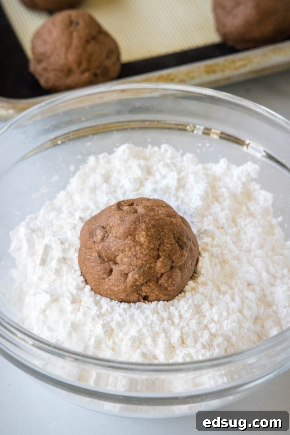 Chocolate snowball cookies are a fun twist on Mexican wedding cookies! These soft chocolate cookies are quick to make and irresistibly fudgy. A warm chocolate cookie being rolled in a bowl of fluffy powdered sugar, creating its signature snowy coating.