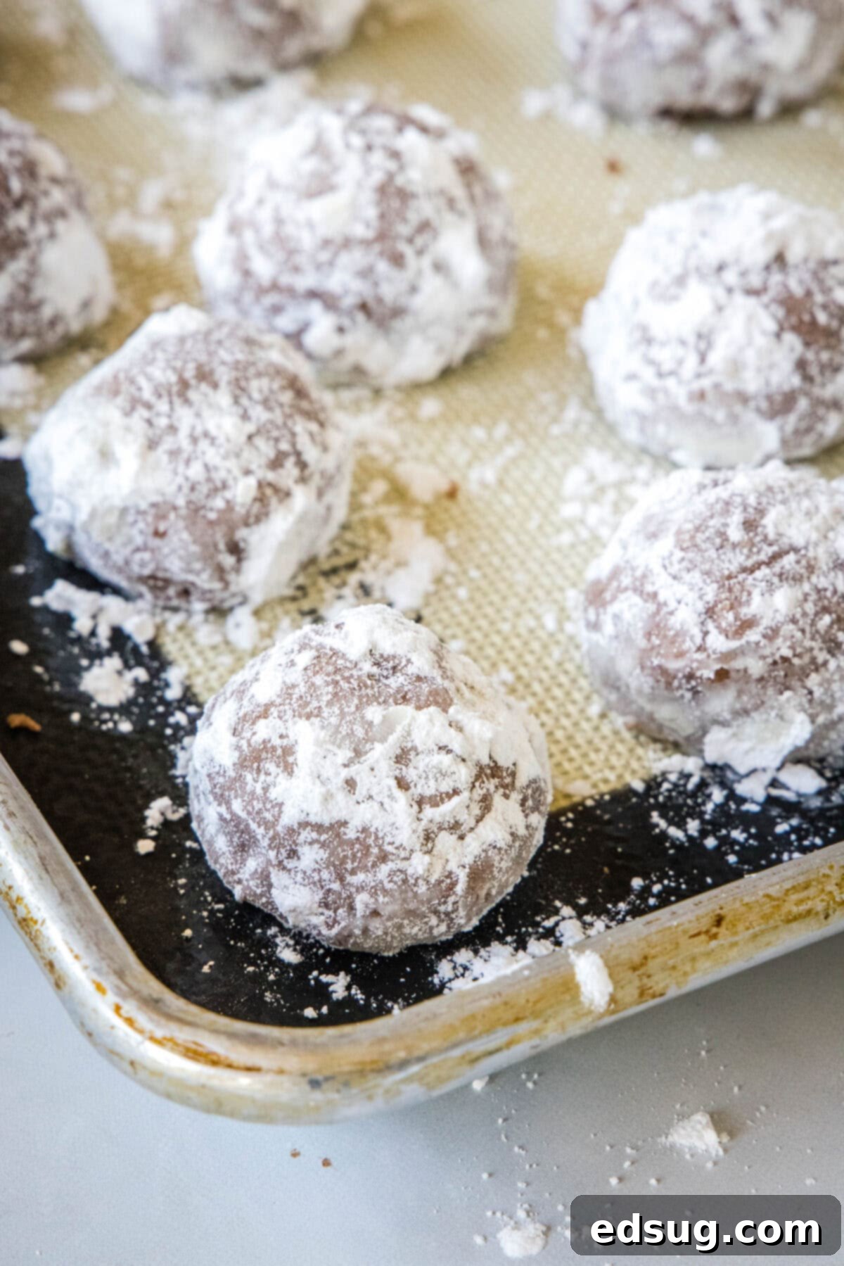 Chocolate snowball cookies are a fun twist on Mexican wedding cookies! These soft chocolate cookies are quick to make and irresistibly fudgy. Freshly dusted chocolate snowball cookies arranged on a silpat-lined baking sheet, sparkling with powdered sugar.