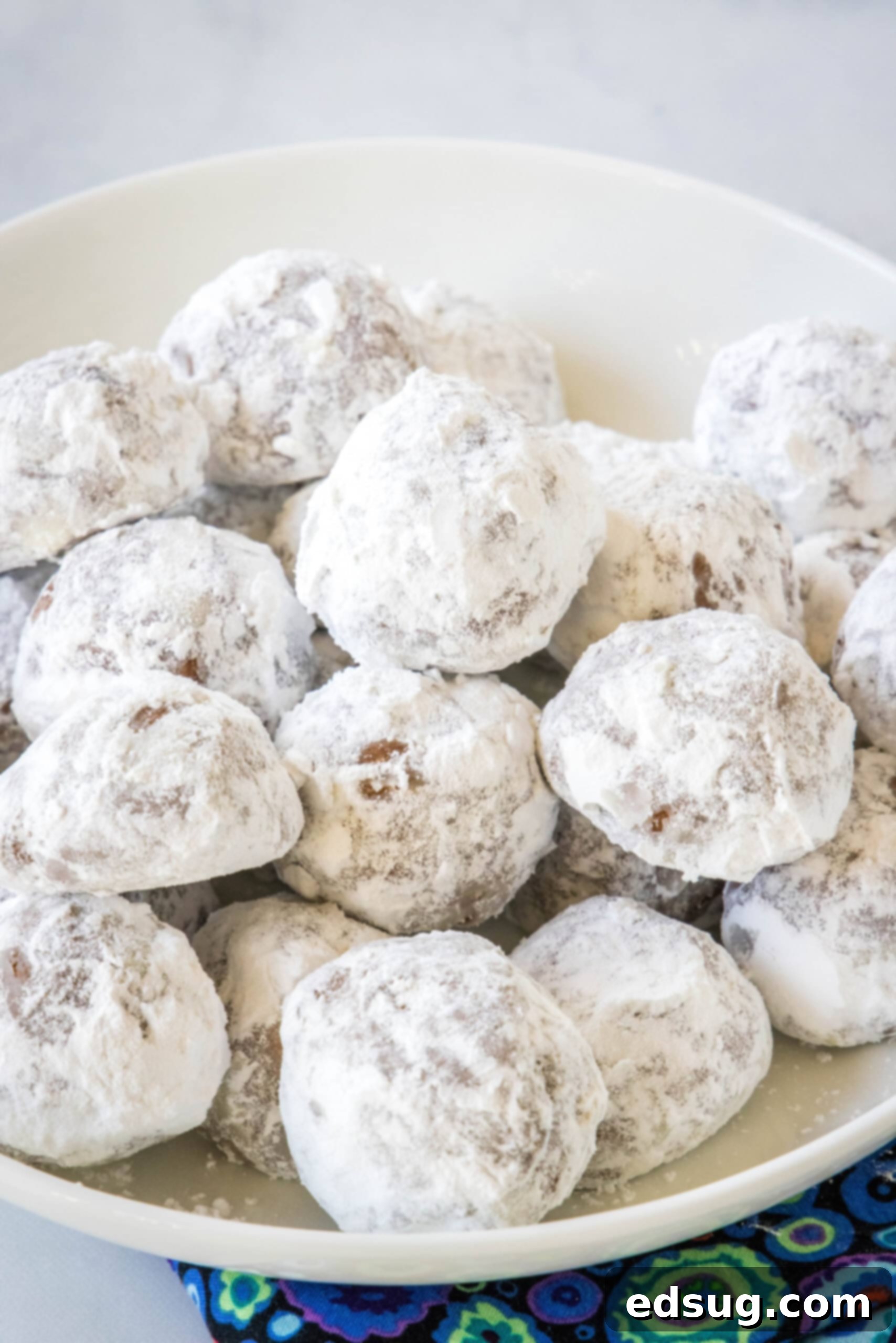 Chocolate snowball cookies are a fun twist on Mexican wedding cookies! These soft chocolate cookies are quick to make and irresistibly fudgy. A beautiful pile of finished chocolate snowball cookies on a white platter, generously dusted with powdered sugar.