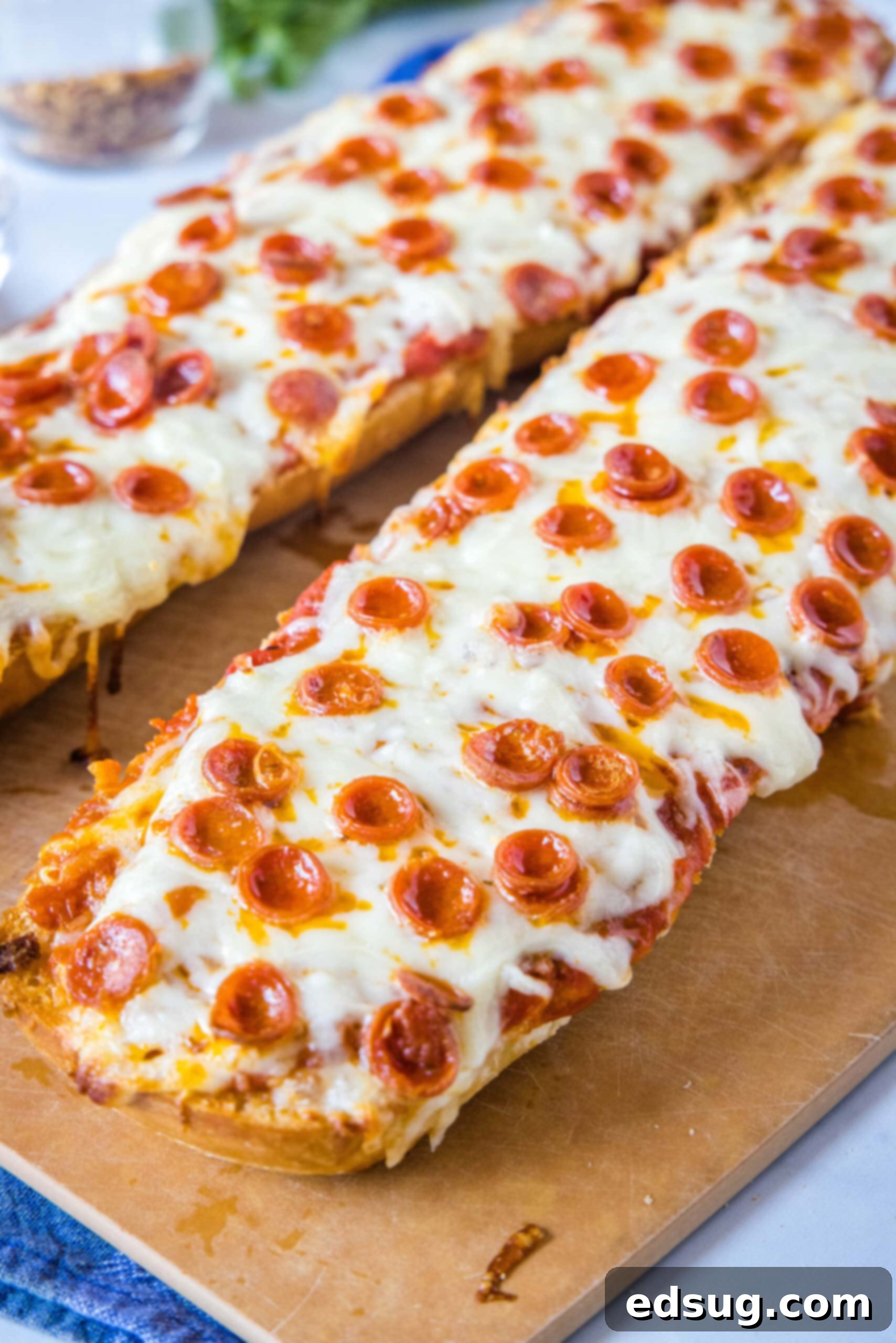 Savor these easy French bread pizzas, fresh out of the oven, with a zesty garlic butter crust, savory pizza sauce, melty mozzarella, and personalized toppings! Two golden-brown French bread pizzas, freshly baked and placed side by side on a rustic wooden cutting board.